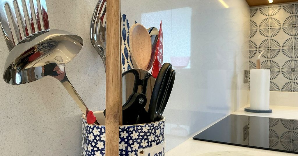 A kitchen countertop with a ceramic utensil holder filled with various cooking utensils such as spatulas, a ladle, and wooden spoons.