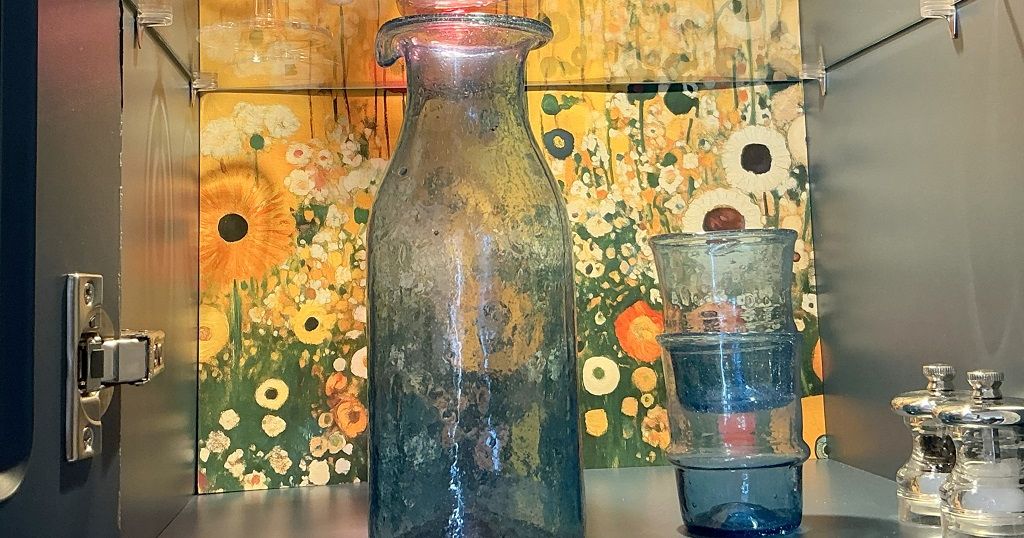 Glassware displayed in a cabinet with a floral artwork background