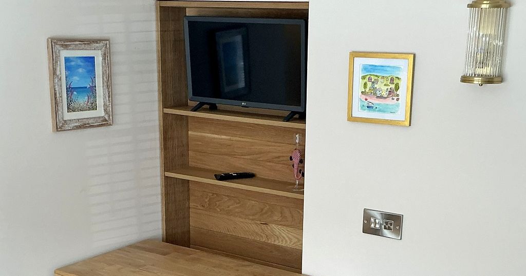 Small wooden table with two stools, wall-mounted TV and art paintings in a cozy nook