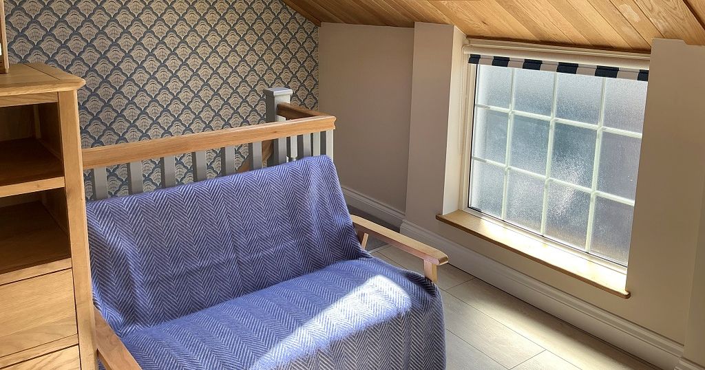 Cozy attic bedroom corner with wooden chair, skylight window, and patterned wallpaper