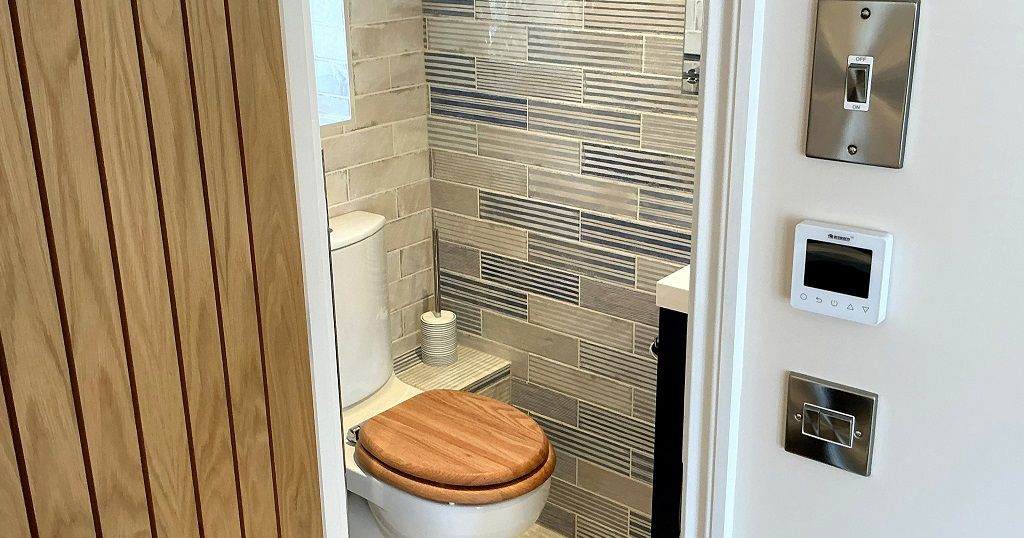 Modern bathroom with a toilet, wooden toilet seat, tiled walls, and a partially open wooden door