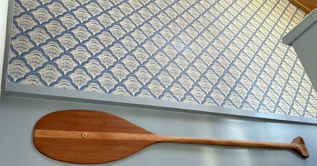 Wooden paddle mounted on a wall below patterned wallpaper and a light fixture