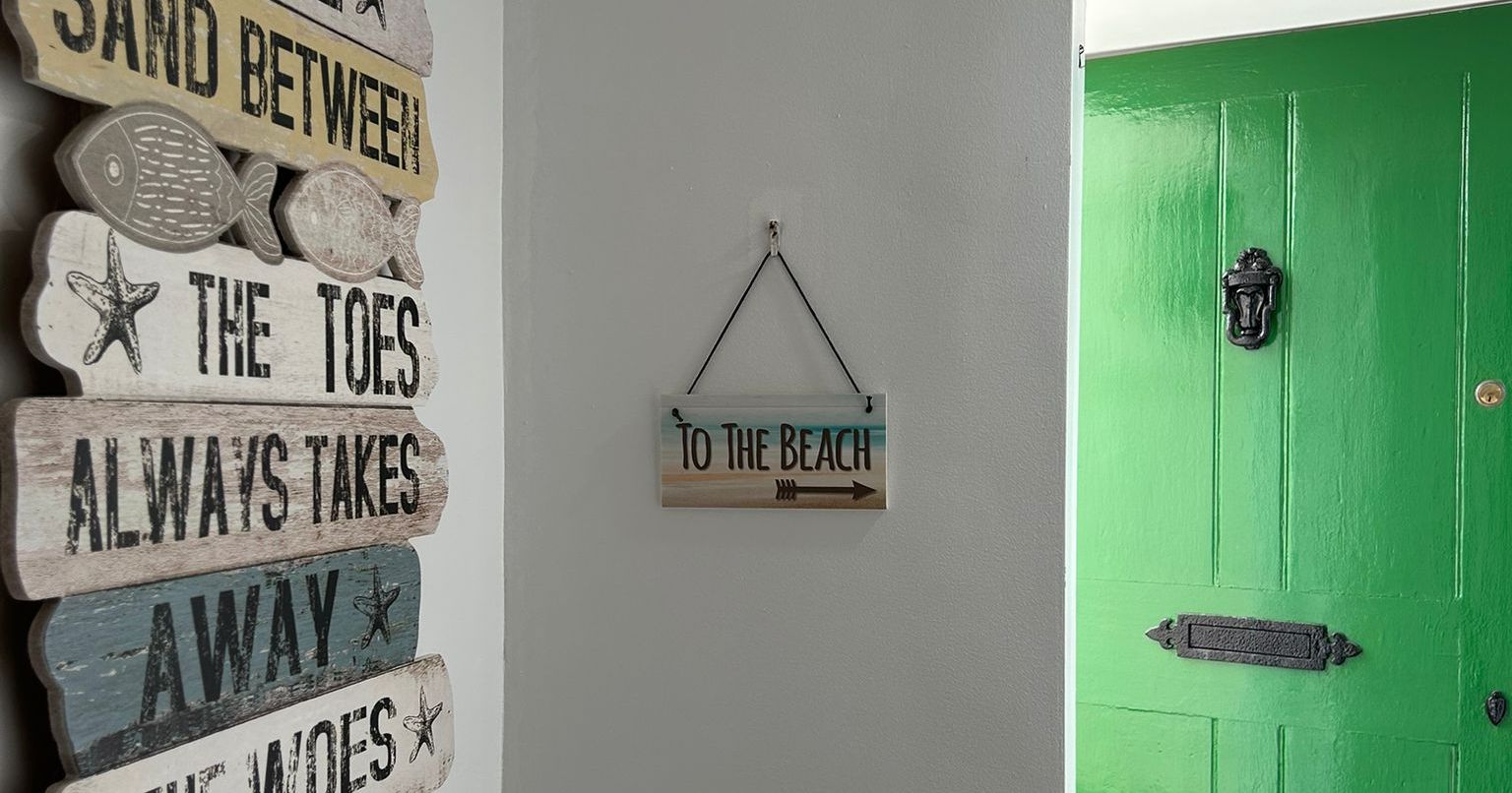 Decorative beach-themed signs on a white wall with a green door open to the outside.