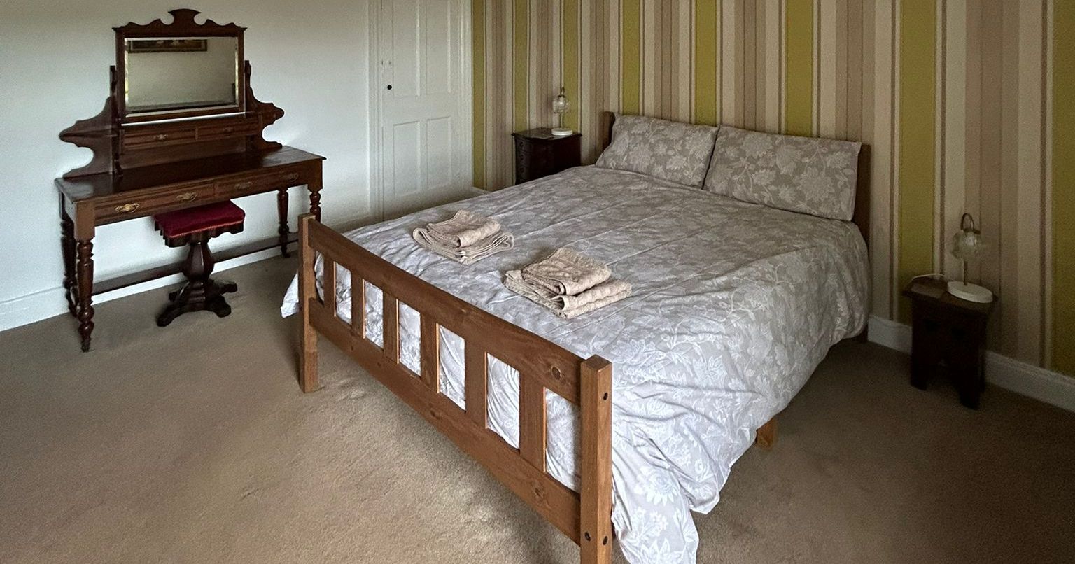 Large bedroom with king-size bed, striped wallpaper, wooden vanity, and yellow ceiling lamp