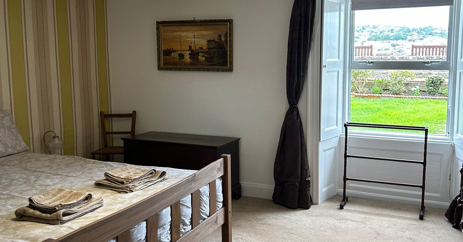 Spacious bedroom with wooden bed, towels, large window, and scenic outdoor view