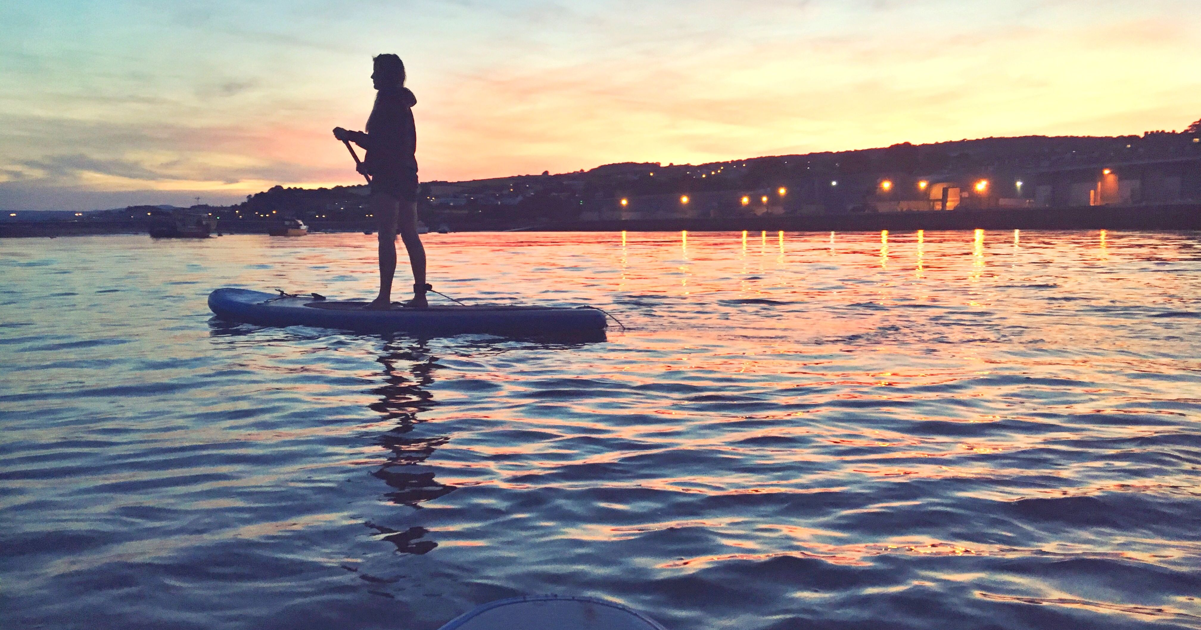 Person paddleboarding on calm water at sunset