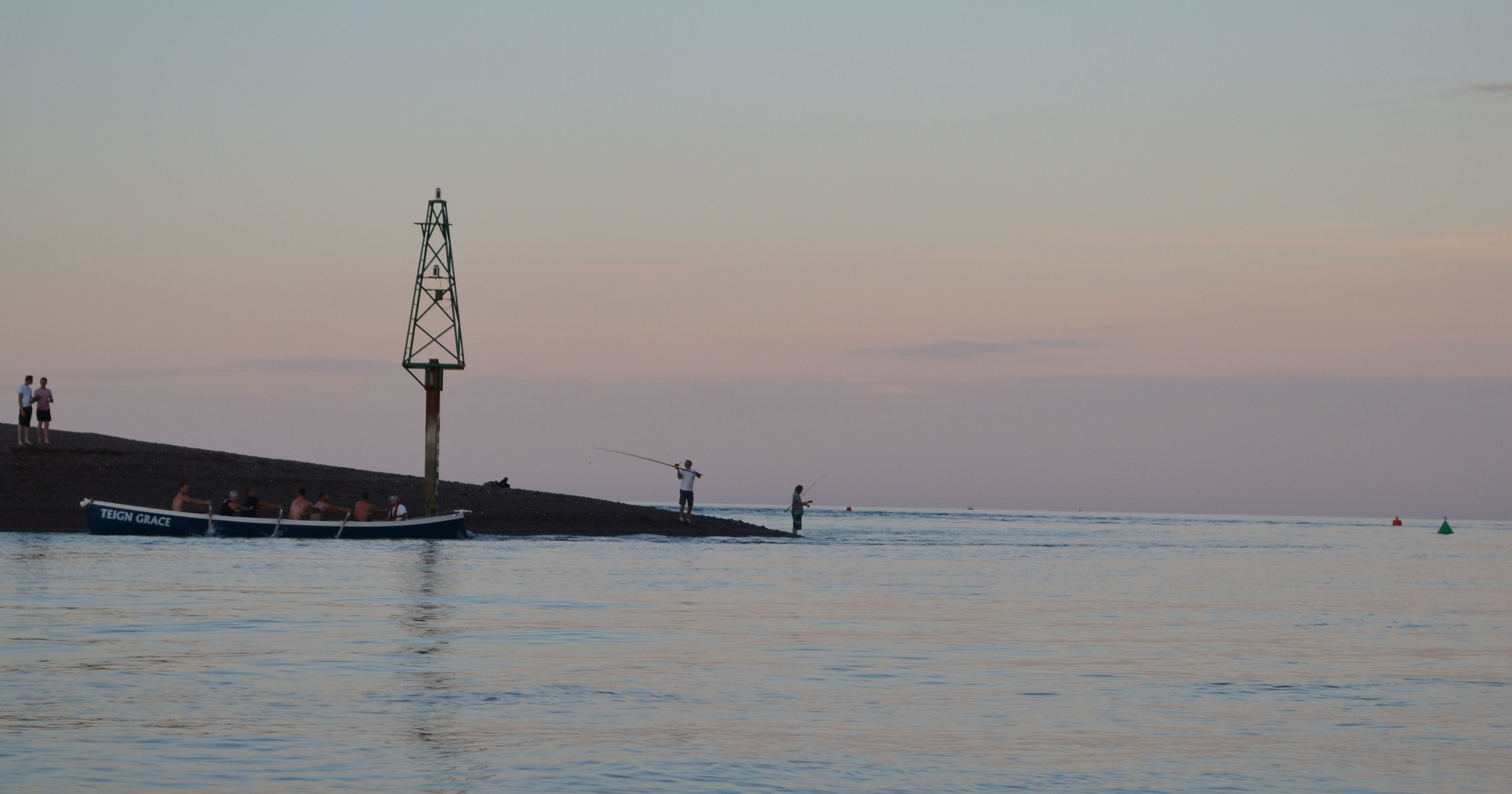 Rowing boat and people fishing by a riverbank at sunset