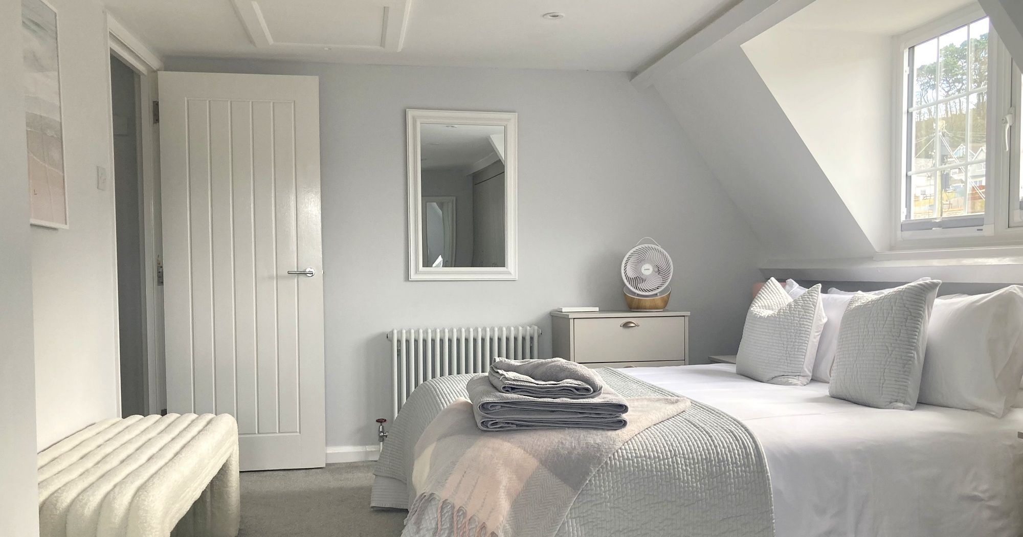 Modern, bright bedroom with a king-sized bed, cozy bench, and a slanted ceiling window.