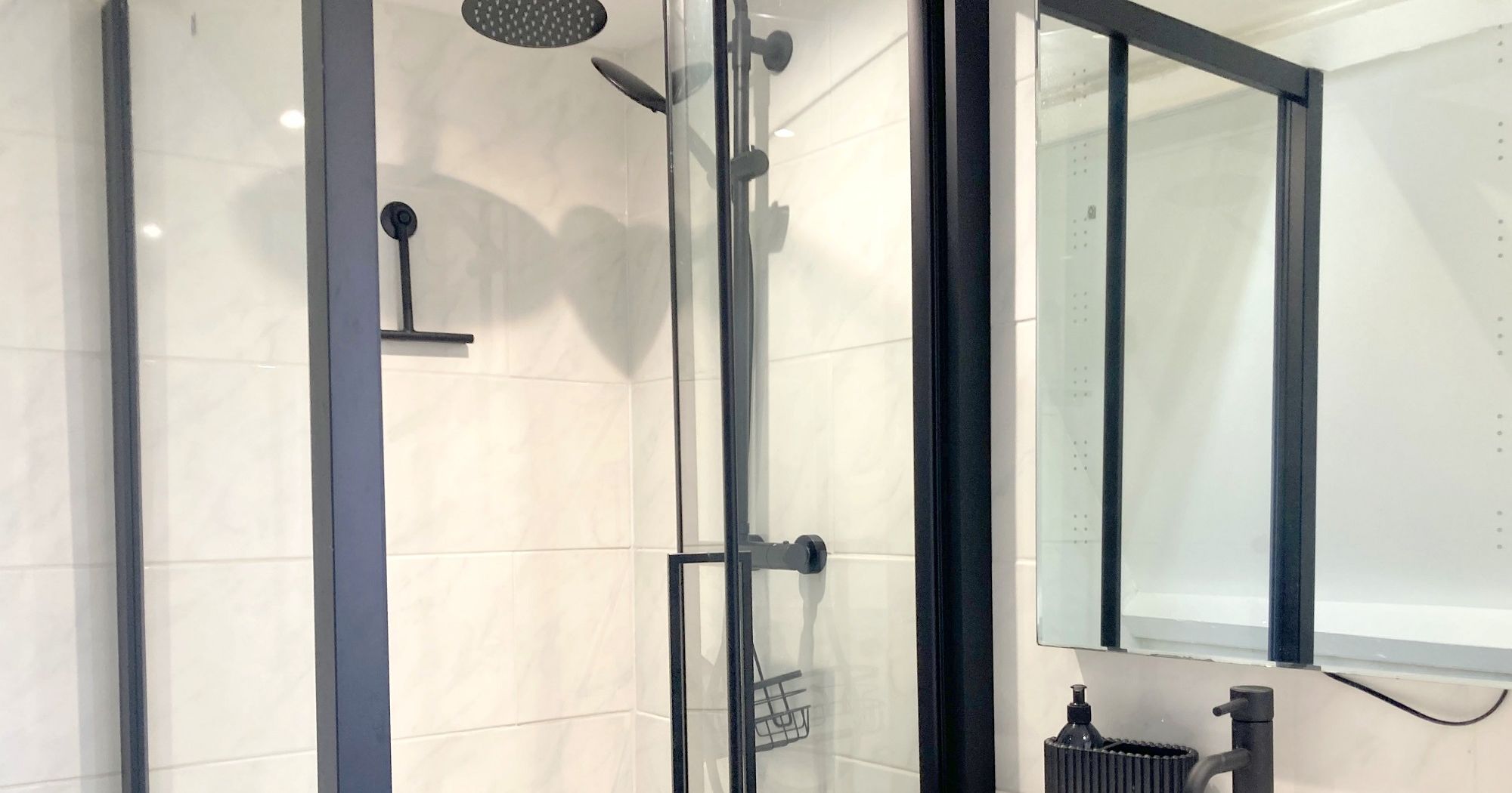Modern bathroom with glass shower enclosure, black fixtures, and vanity with mirror.