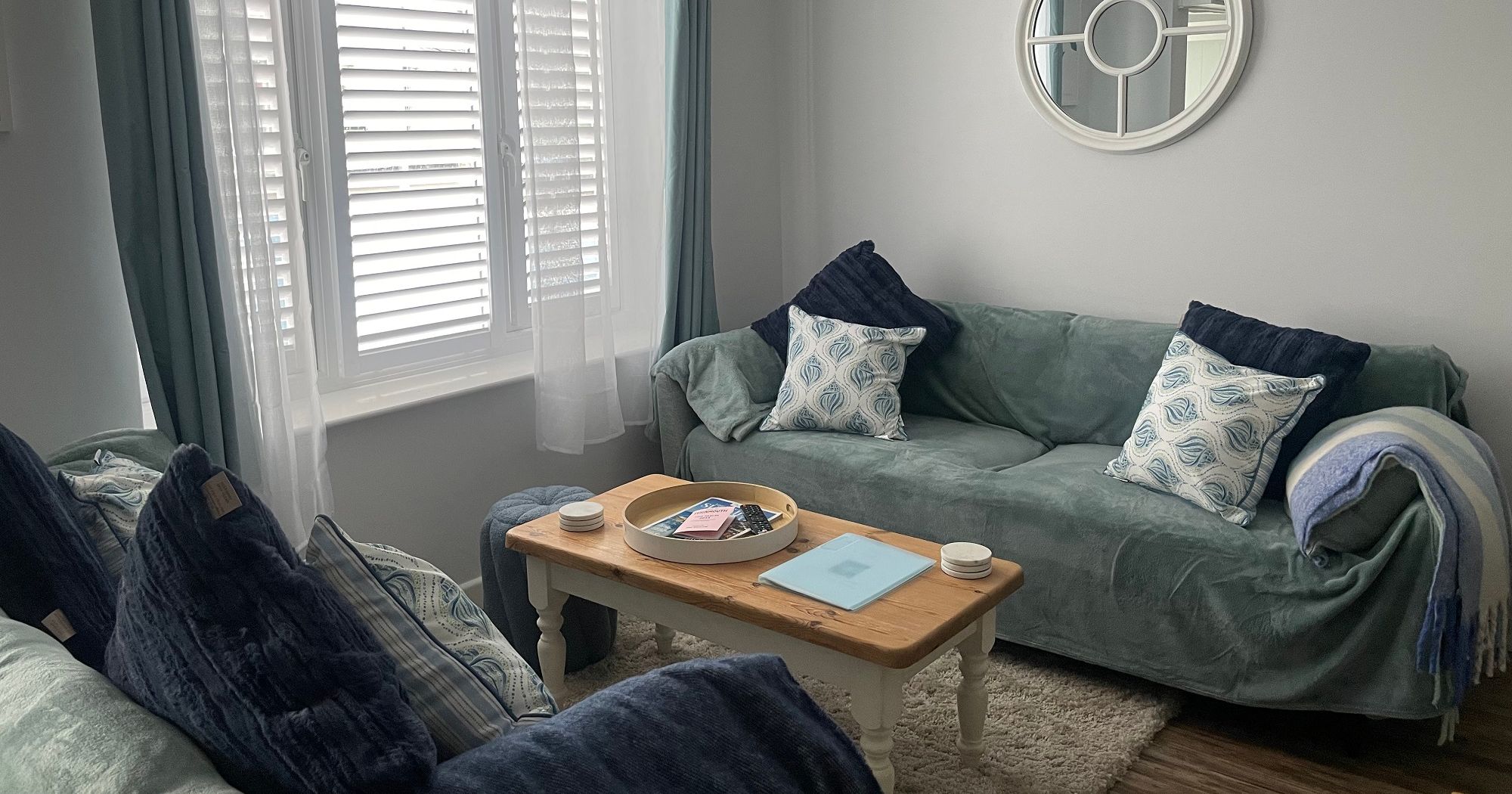 Cozy sitting room with two sofas, a coffee table, window with shutters, and a round wall mirror.