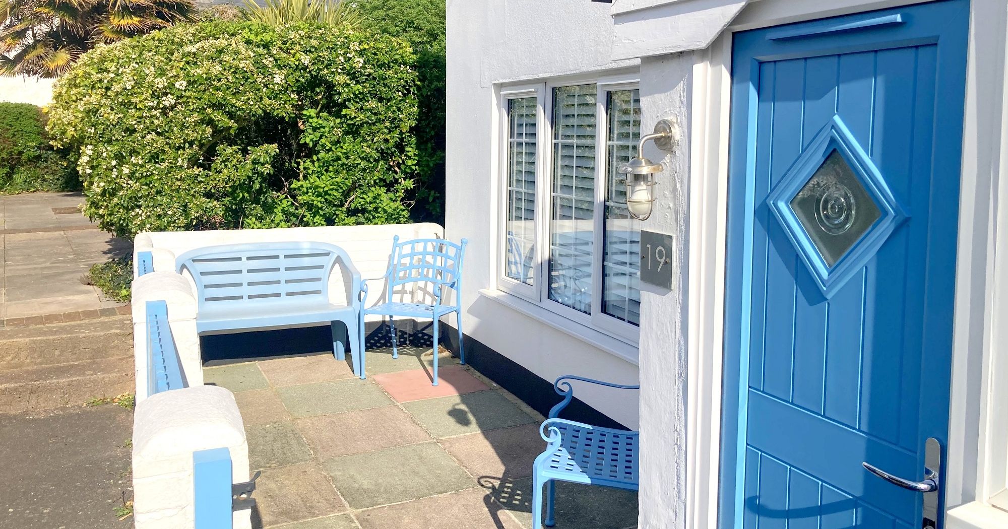 Bright blue front door and outdoor seating area of a white cottage