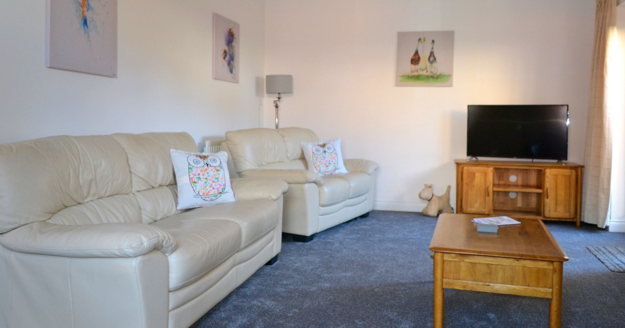 Modern living room with cream leather sofas, wooden coffee table, TV, and animal-themed wall art