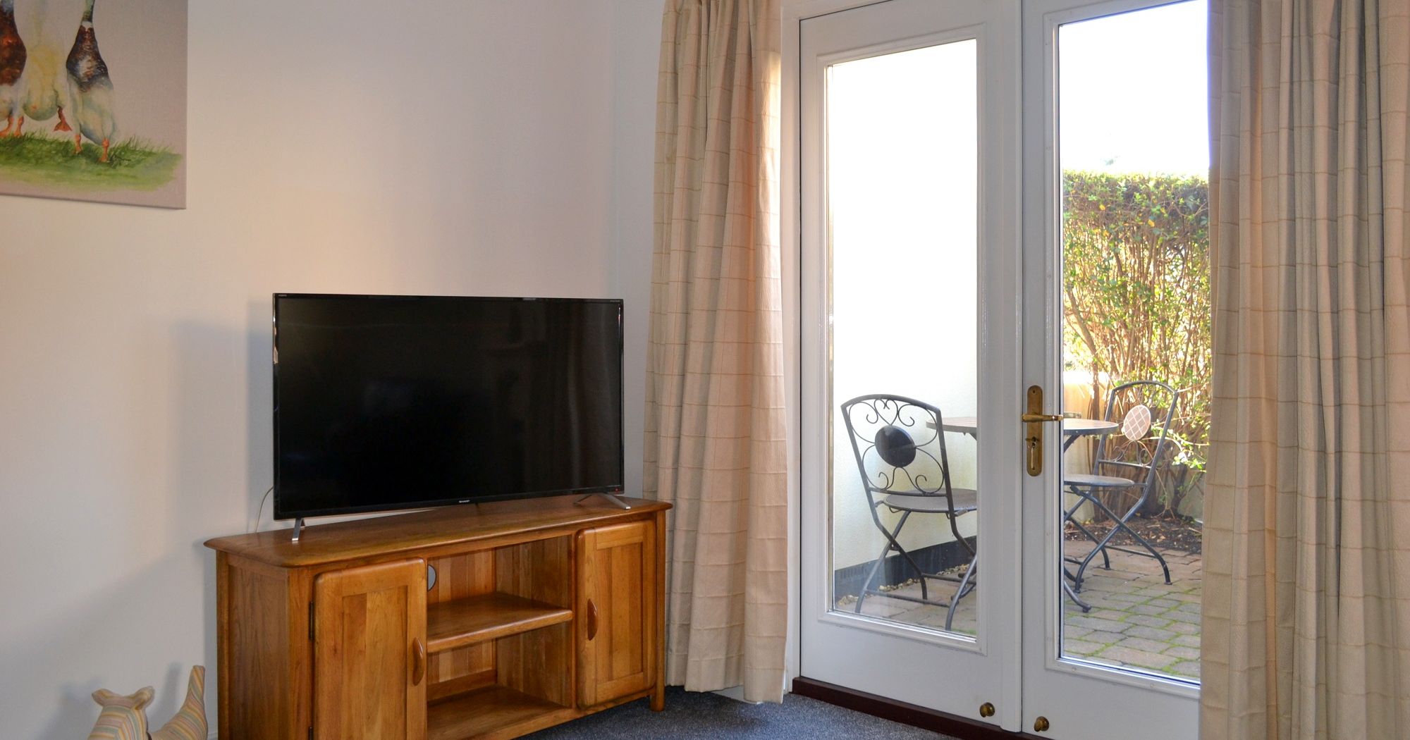 Living room corner with TV on wooden stand, French doors, and patio seating outside