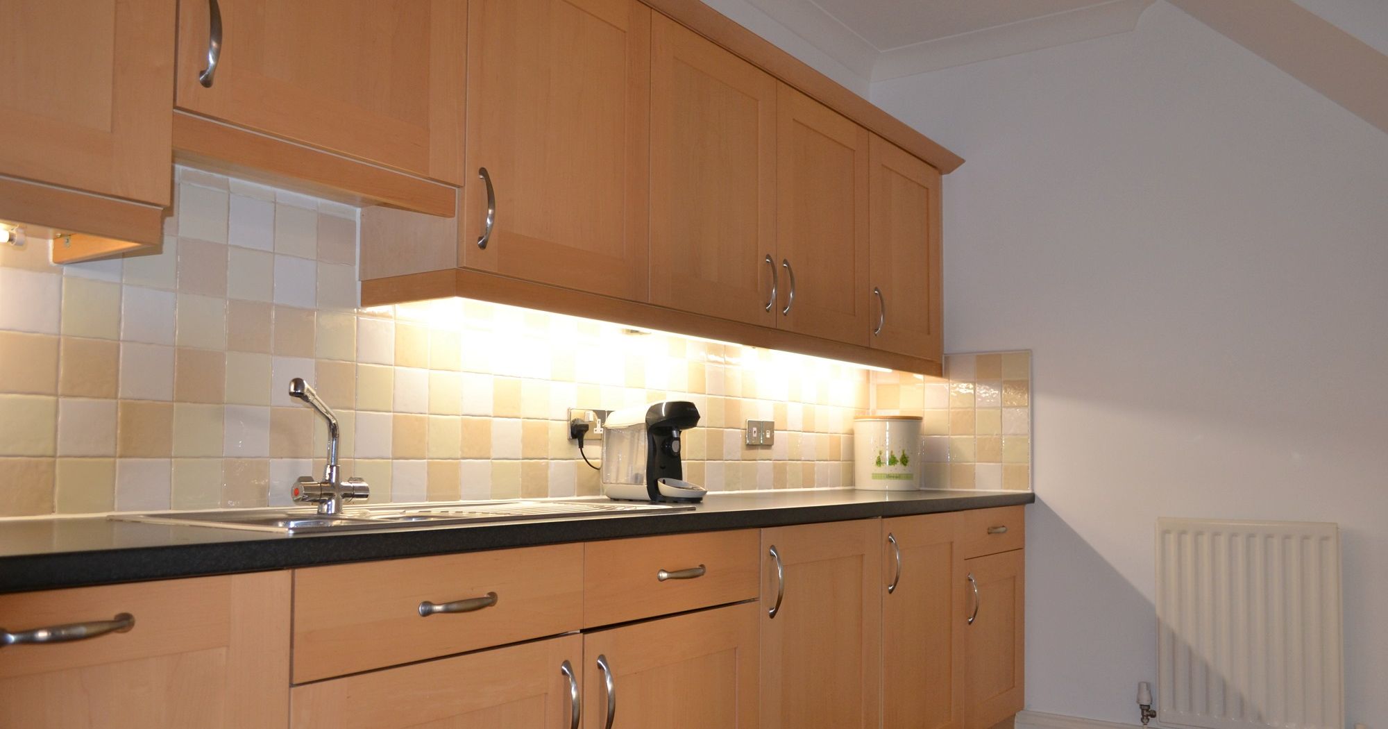 Modern kitchen with light wood cabinets, a countertop, sink, coffee maker, and tiled backsplash.
