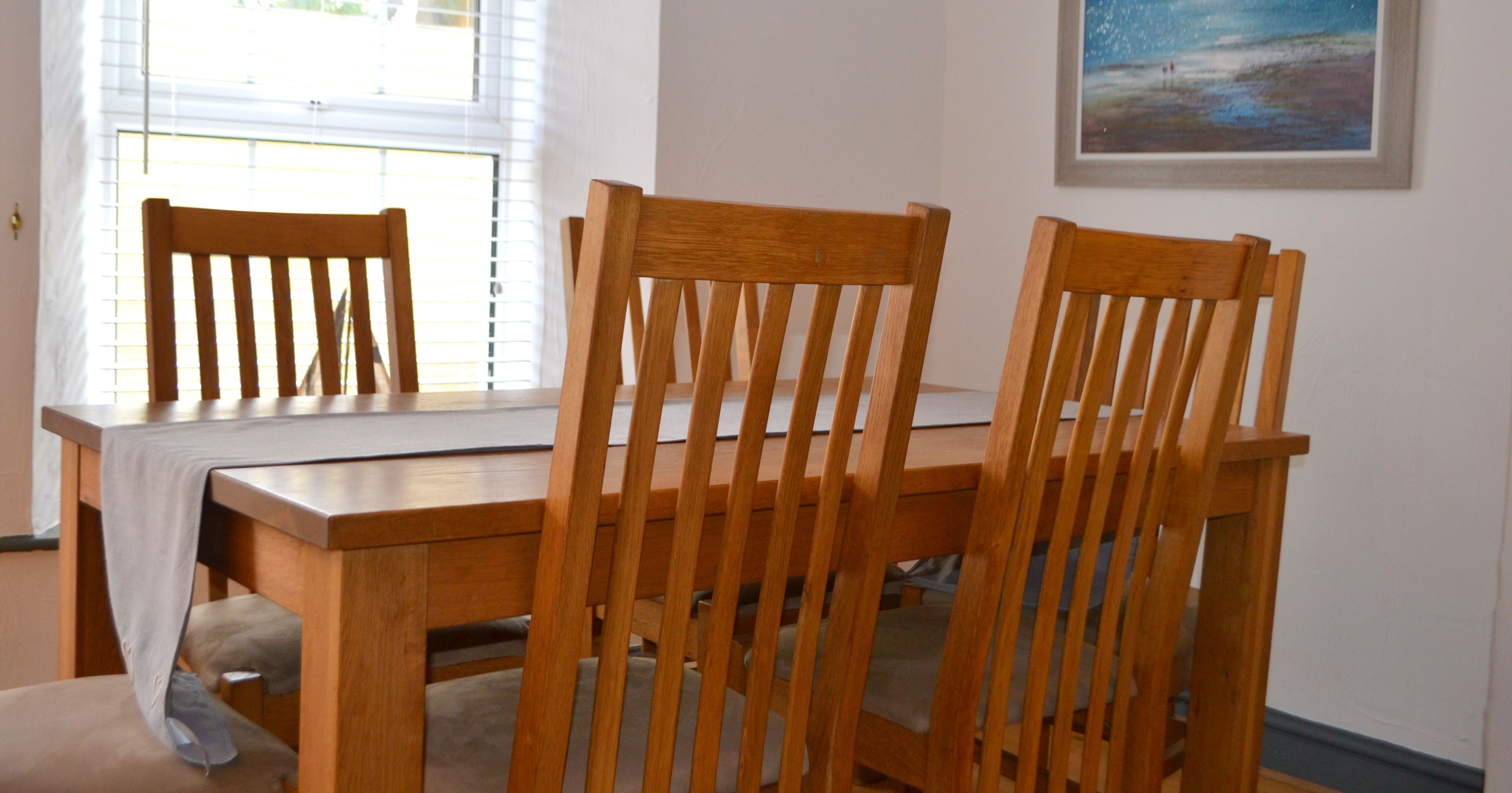 Wooden dining table and chairs in a bright room with a seascape painting on the wall