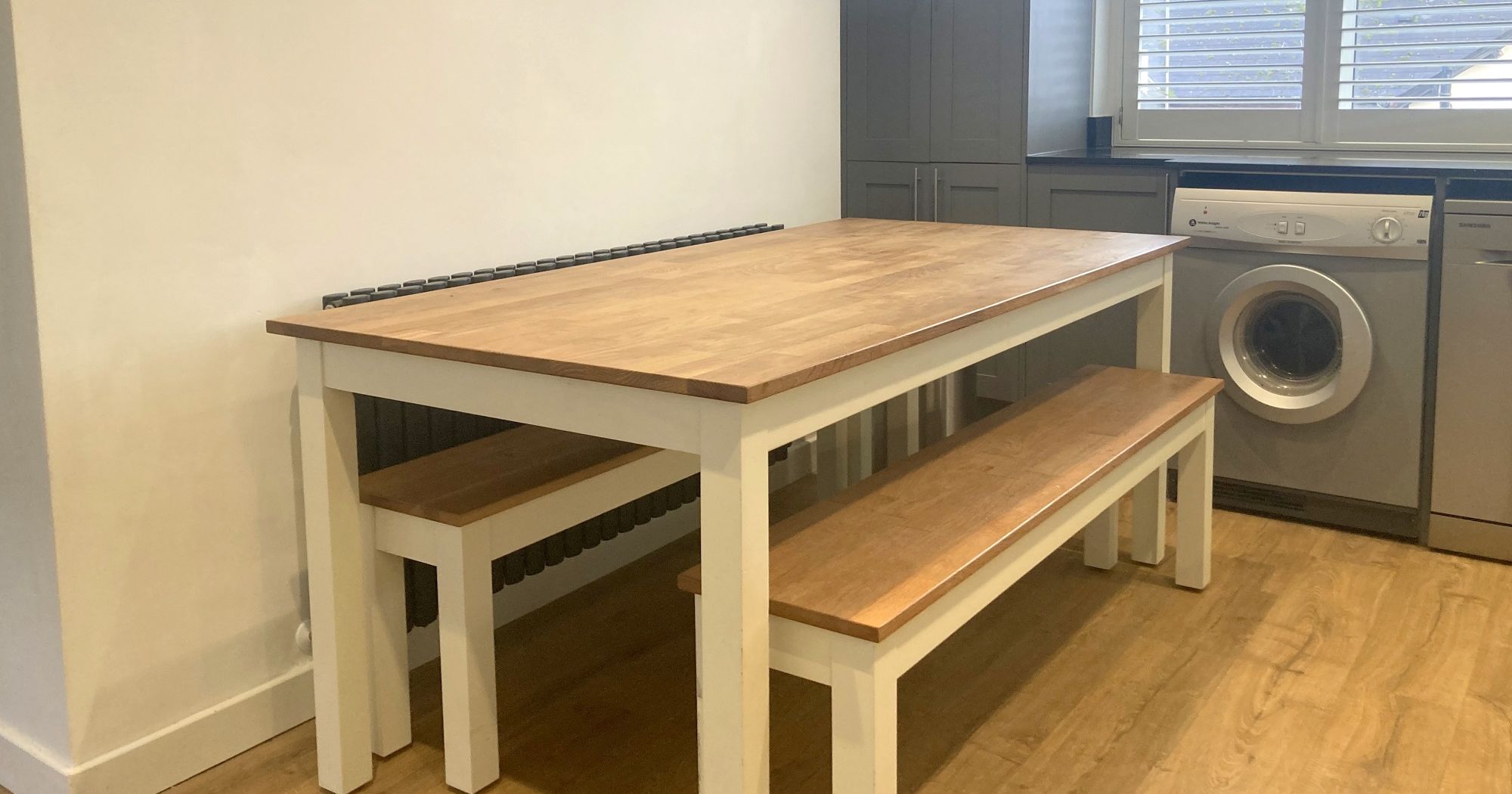 Wooden dining table with benches in a kitchen with a wall clock