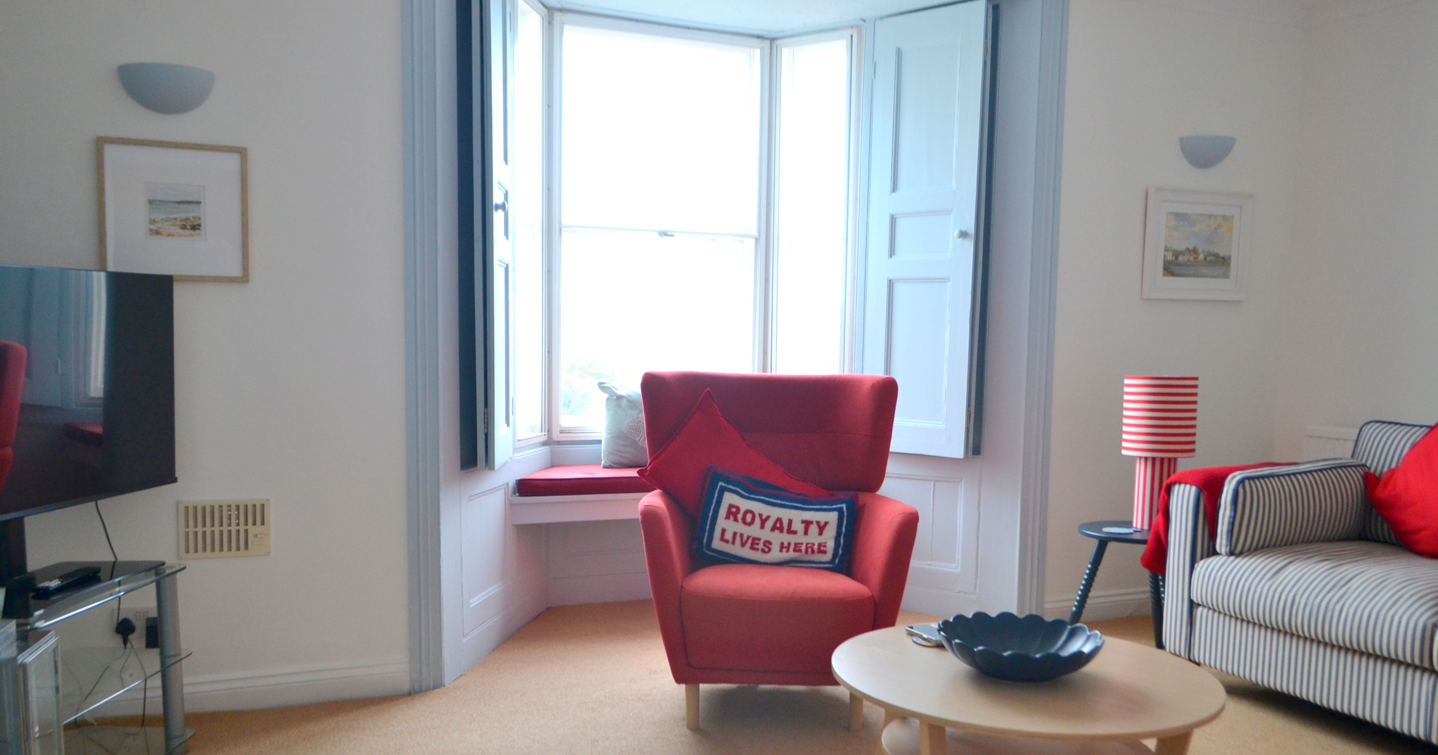 Cozy living room with a red armchair, striped sofa, wooden table, and large bay window