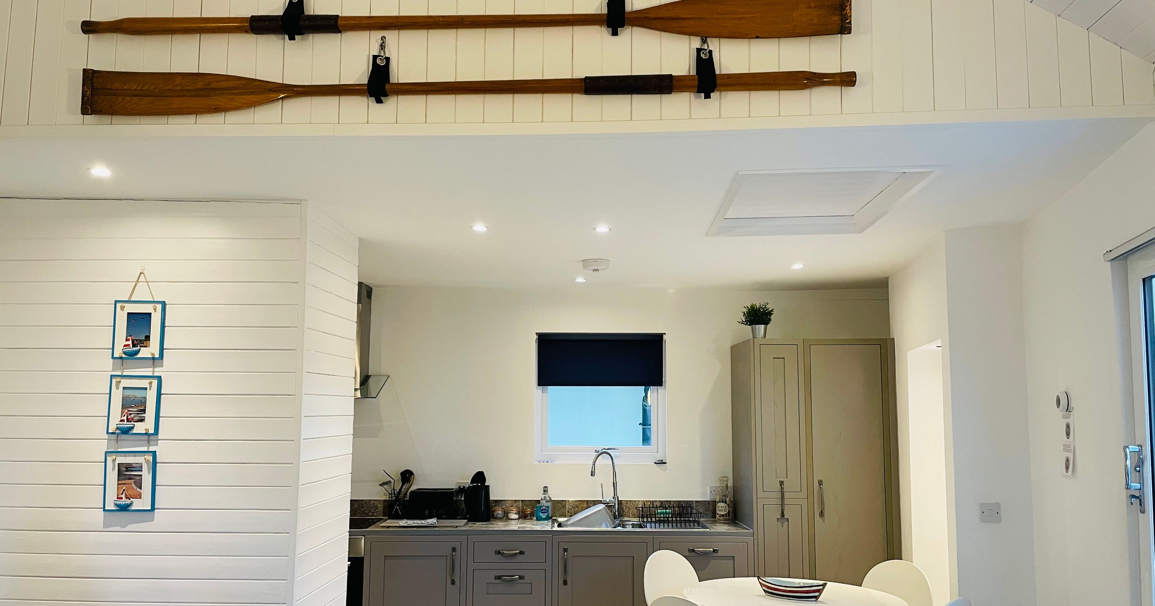 Modern kitchen and dining area with white walls, a round table with four chairs, and wooden oars mounted on the wall above.