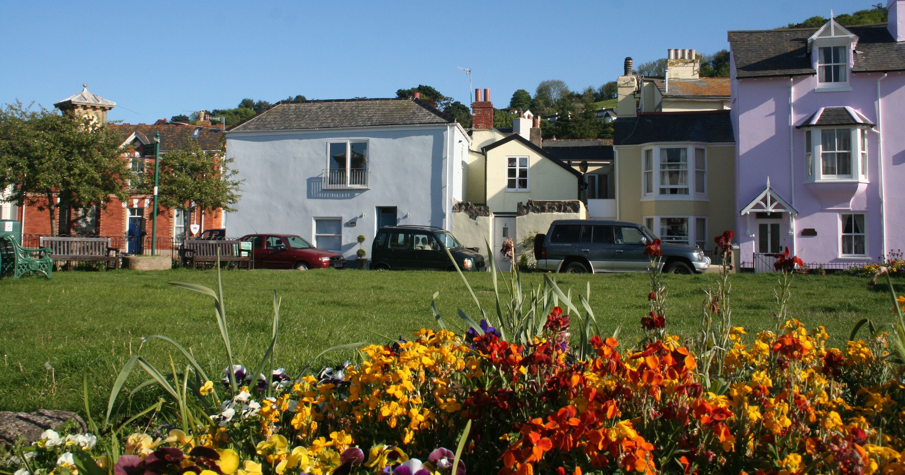 Colorful cottages on The Green in Shaldon, with vibrant flowers in the foreground.
