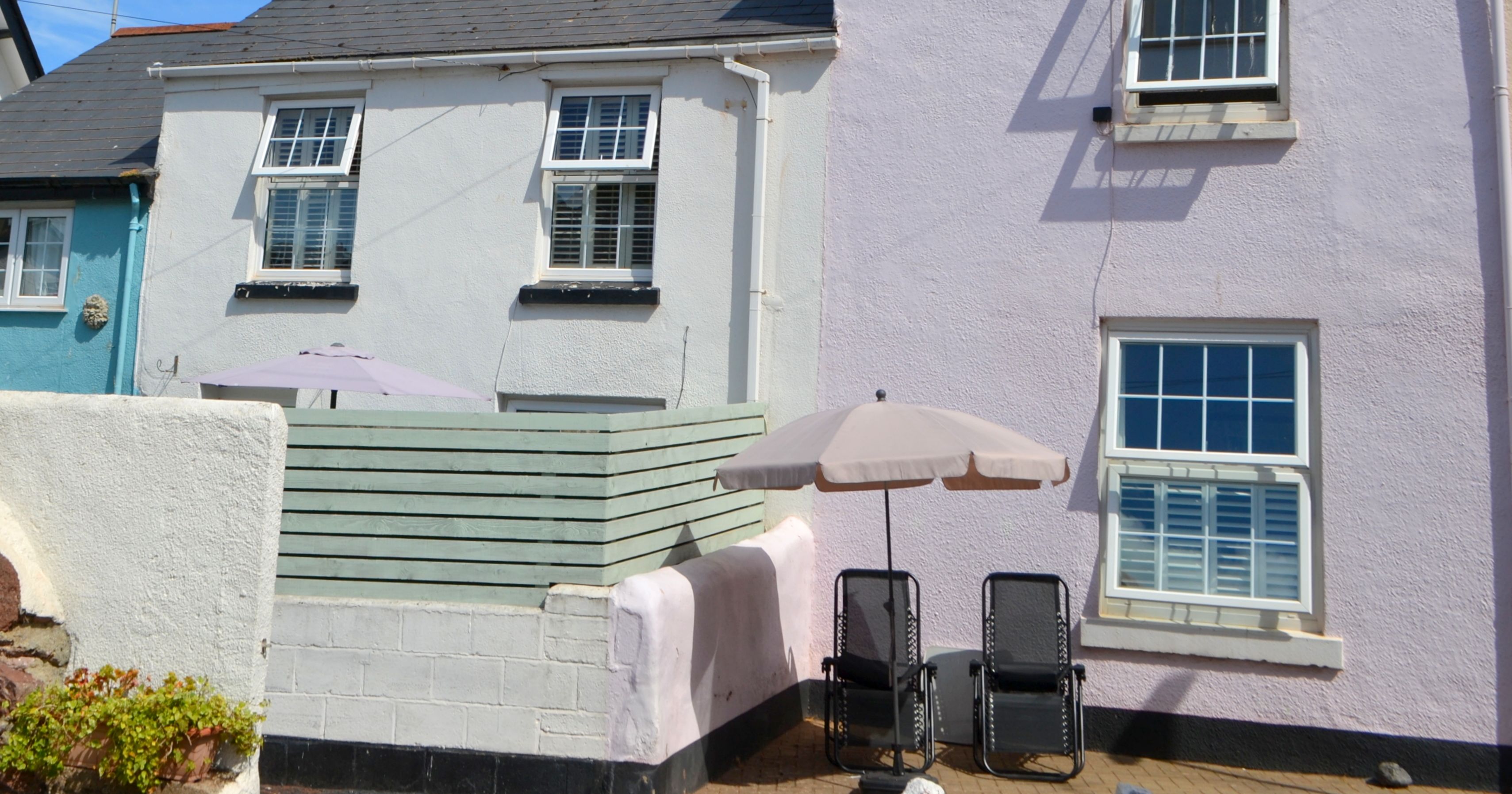 Pastel colored cottage with outdoor seating and umbrellas under a bright blue sky