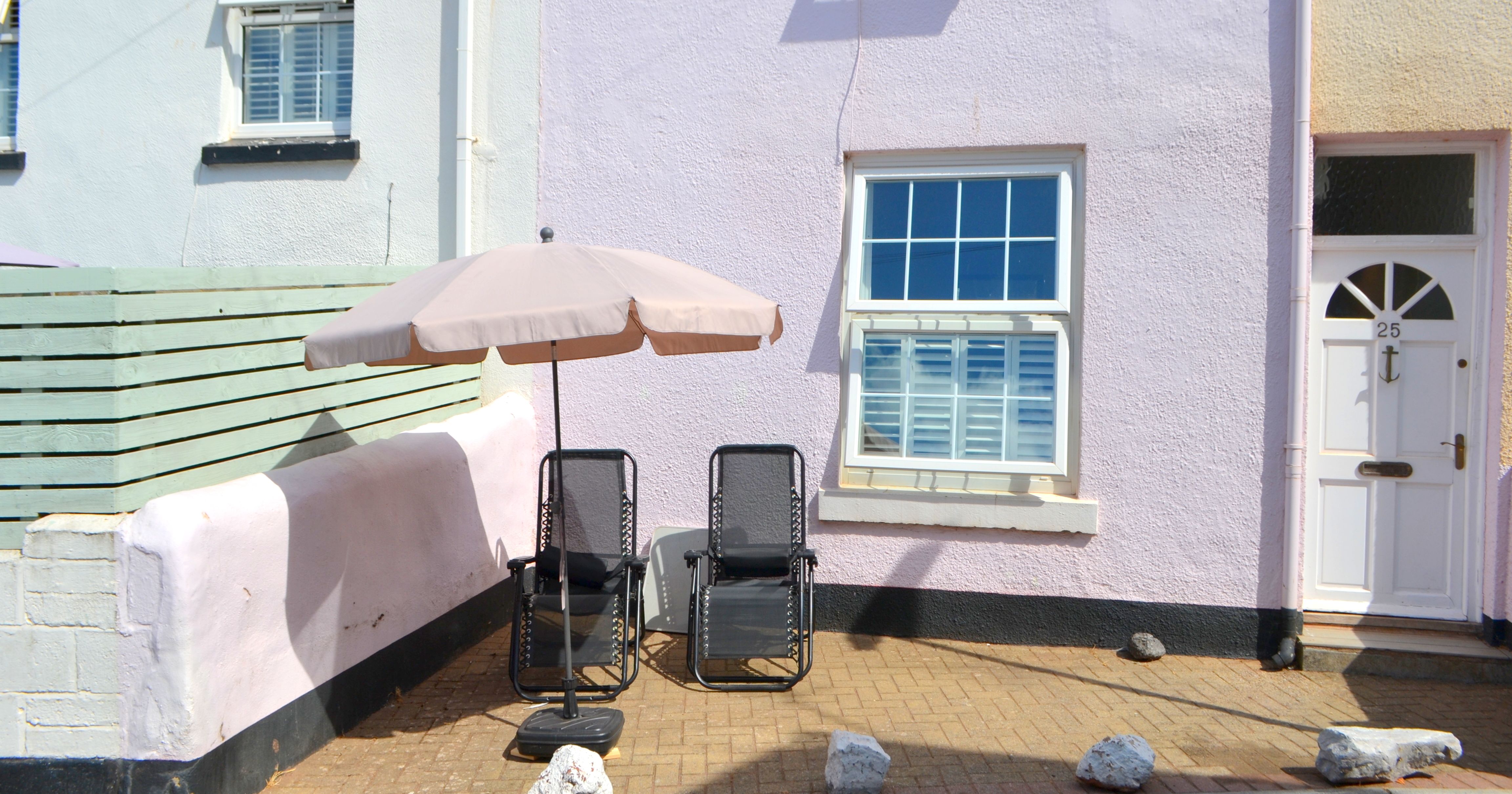 Two lounge chairs and a large umbrella outside a pastel-colored house with the door number 25.