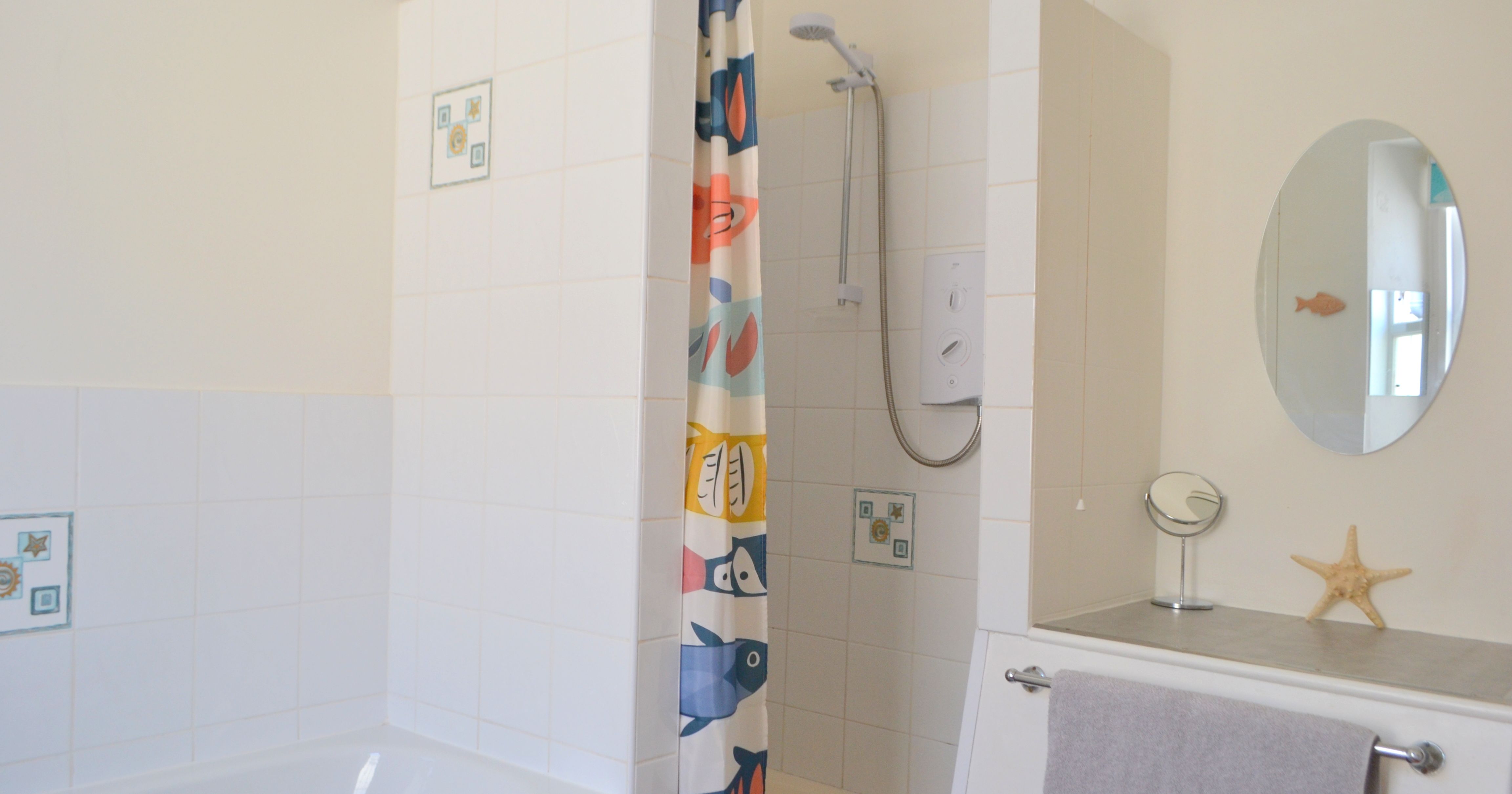 Modern bathroom with shower, bathtub, fish-patterned shower curtain, and aquatic-themed decorations
