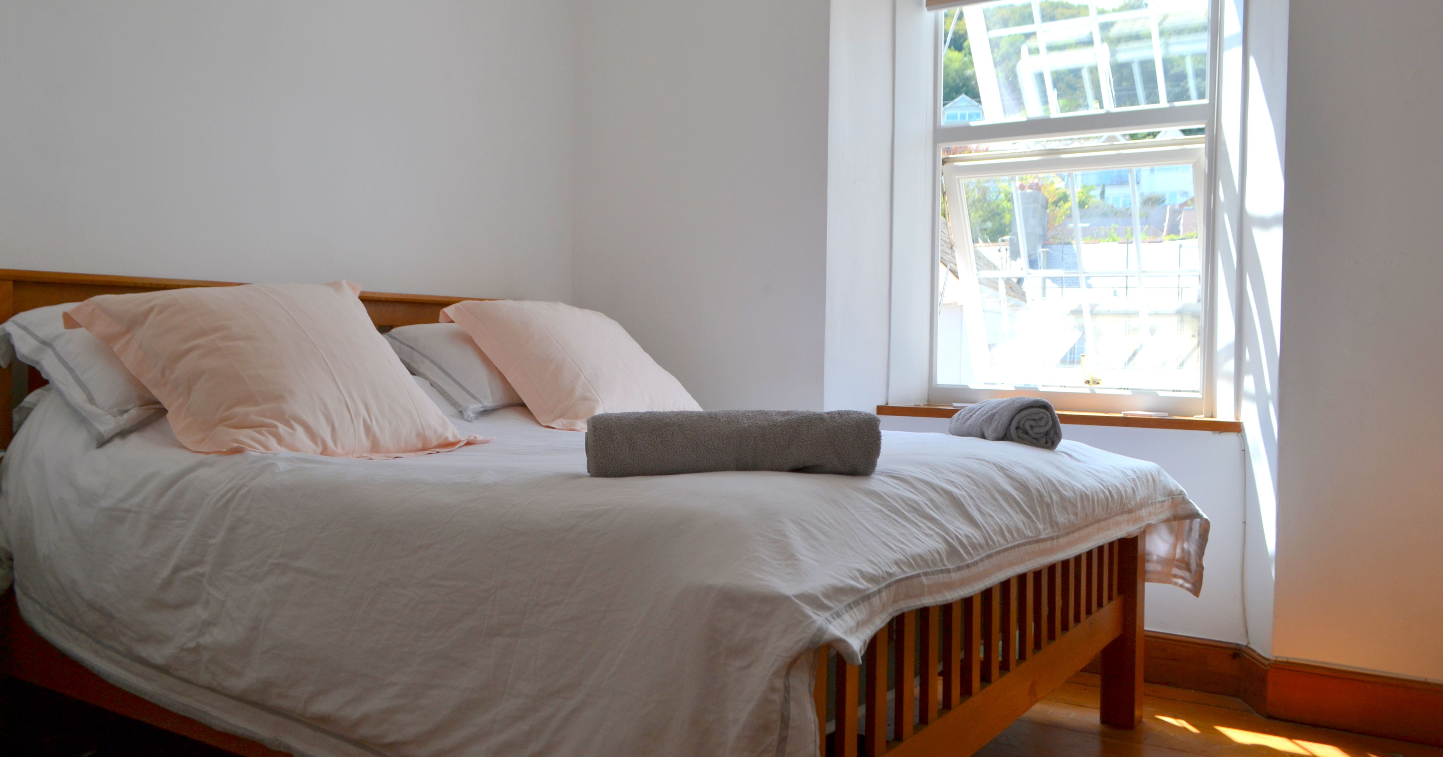 A bright bedroom with a large bed, soft bedding, and pillows near a sunlit window.