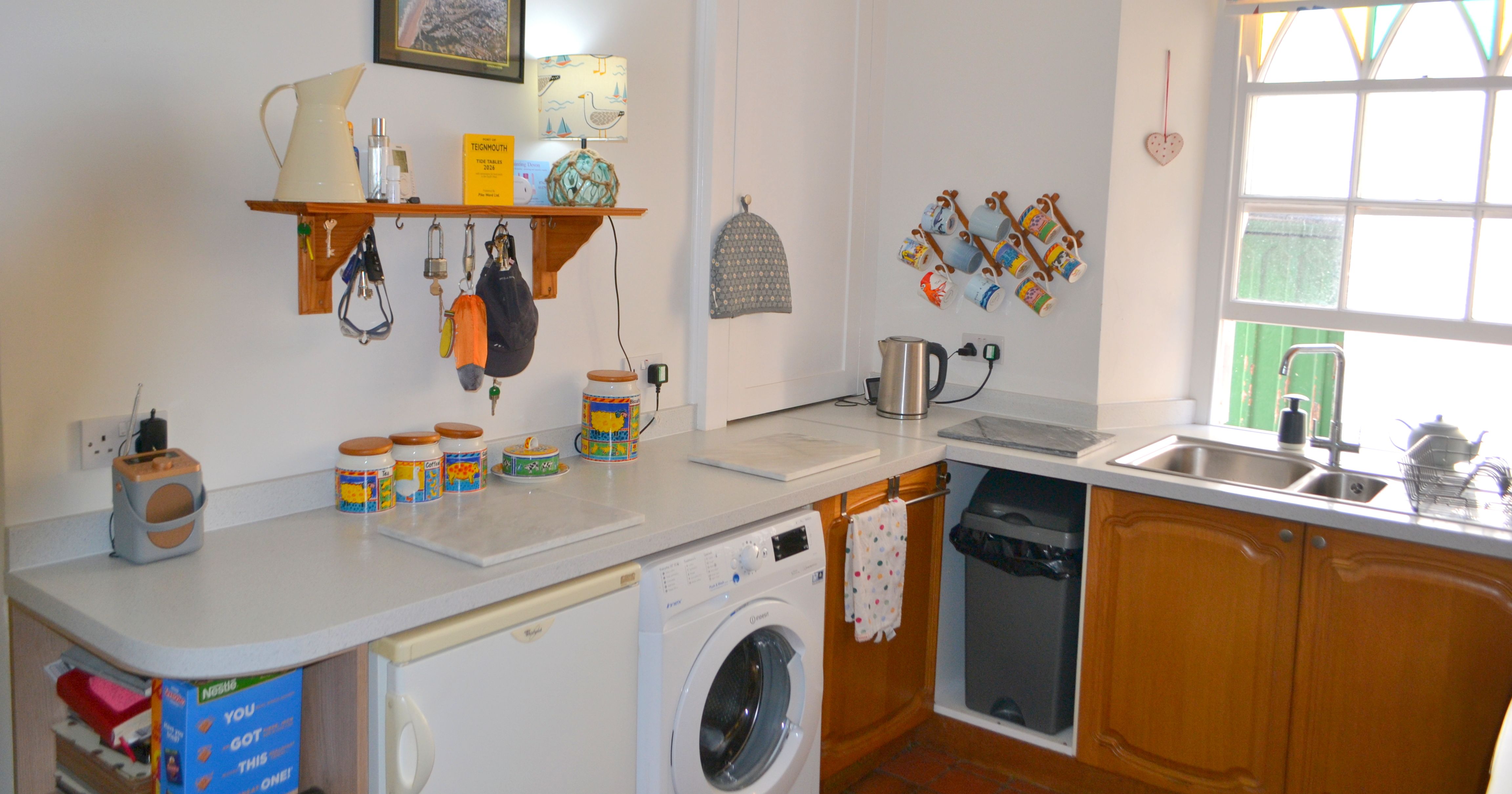 Cozy kitchen with wooden cabinets, countertop appliances, a washing machine, and mugs hanging on the wall.