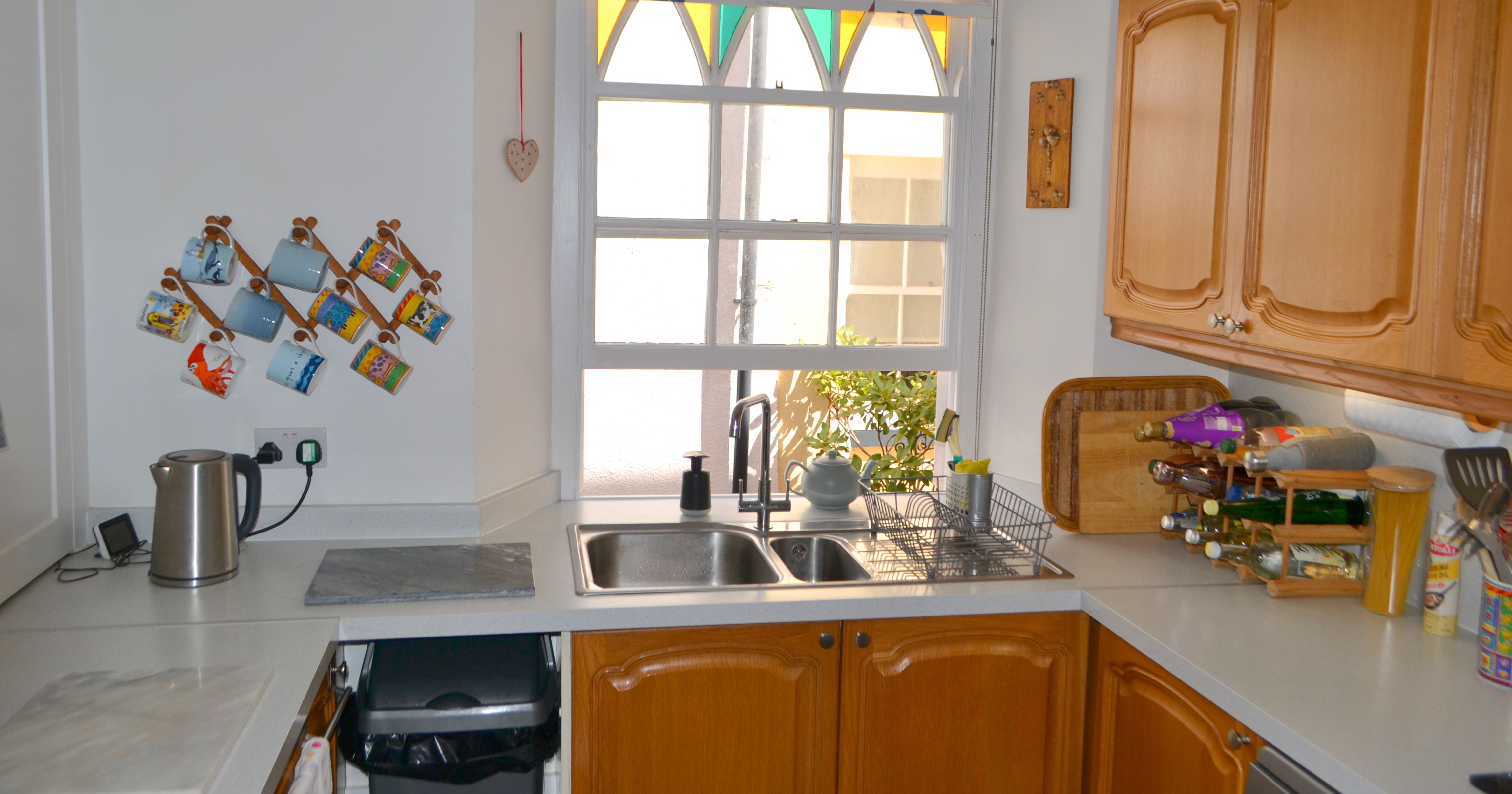 Bright kitchen with wooden cabinets, a window, and countertop items including a dish rack and wine rack.