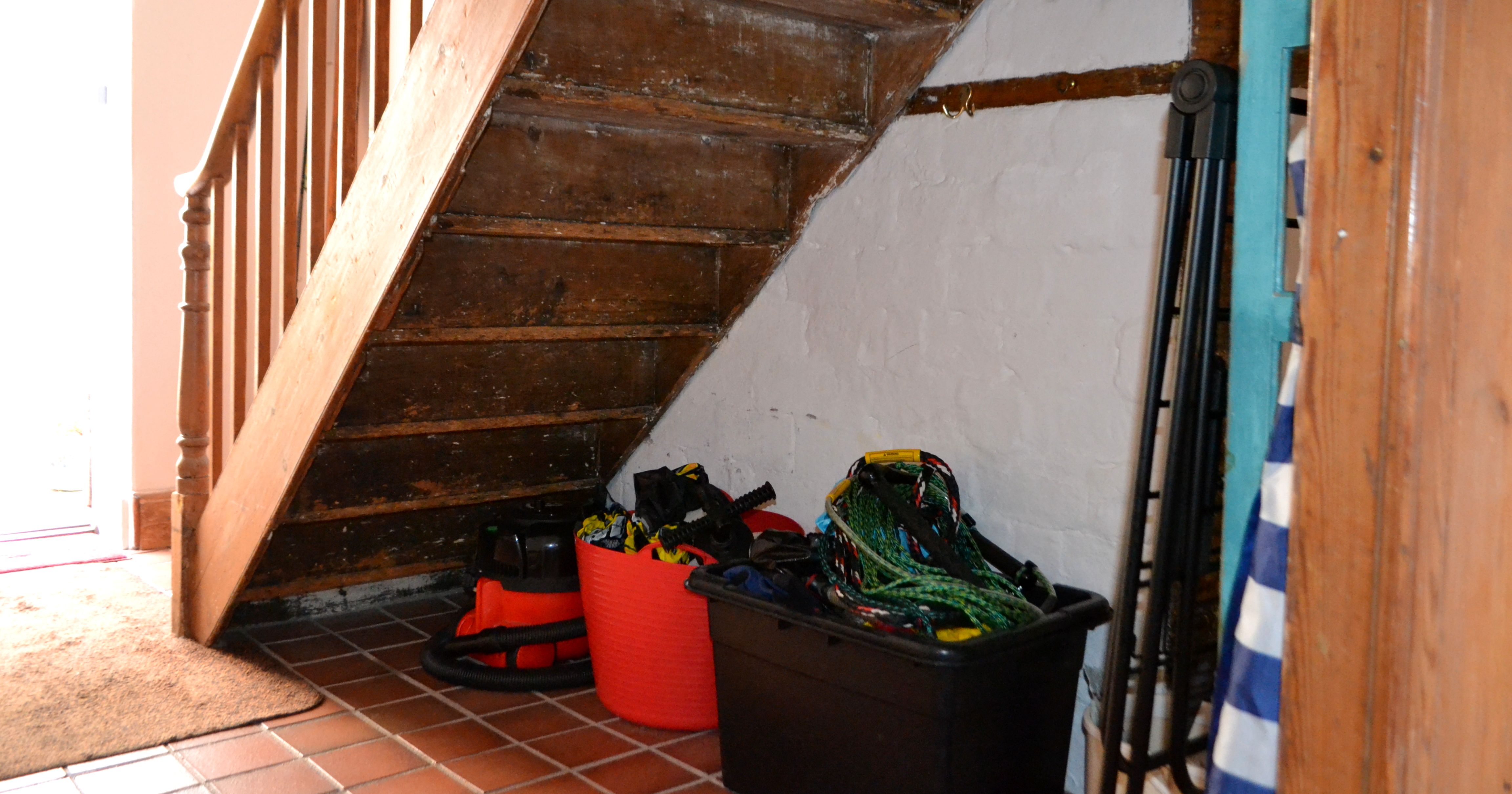 Storage area under wooden staircase with cleaning supplies and bins