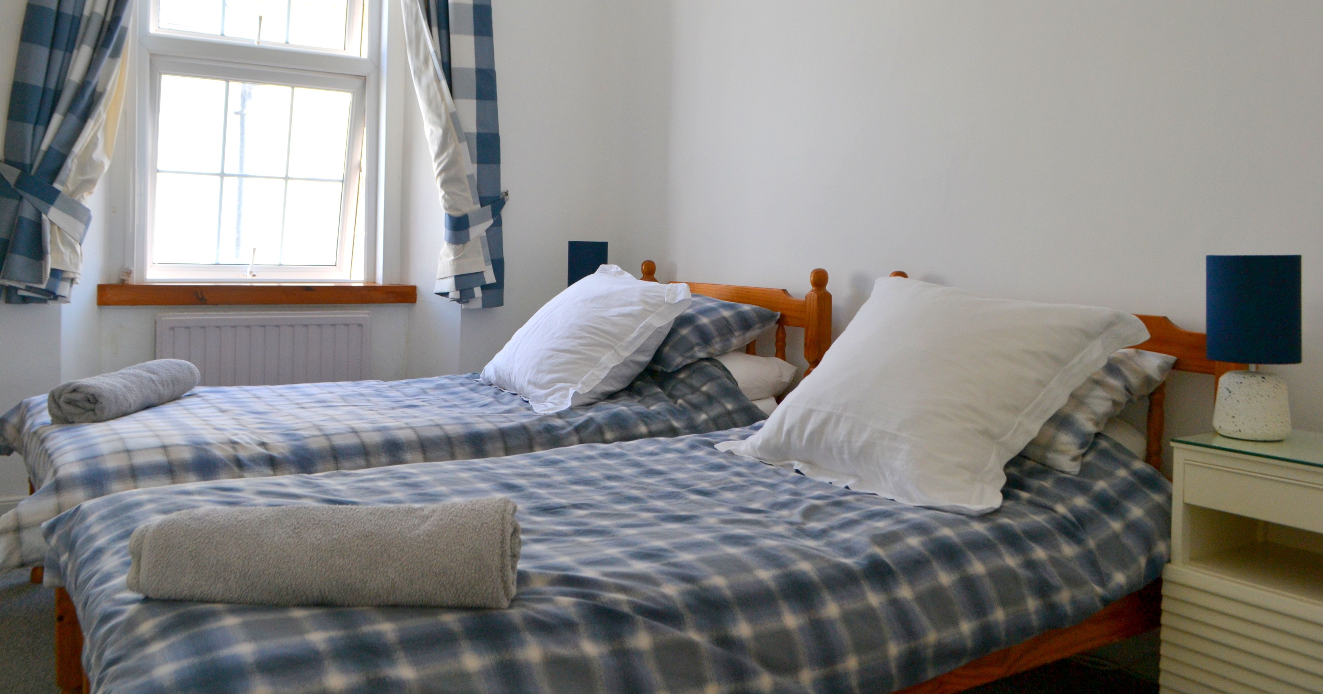 Twin bedroom with two single beds, blue checkered bedding, and a window with matching curtains