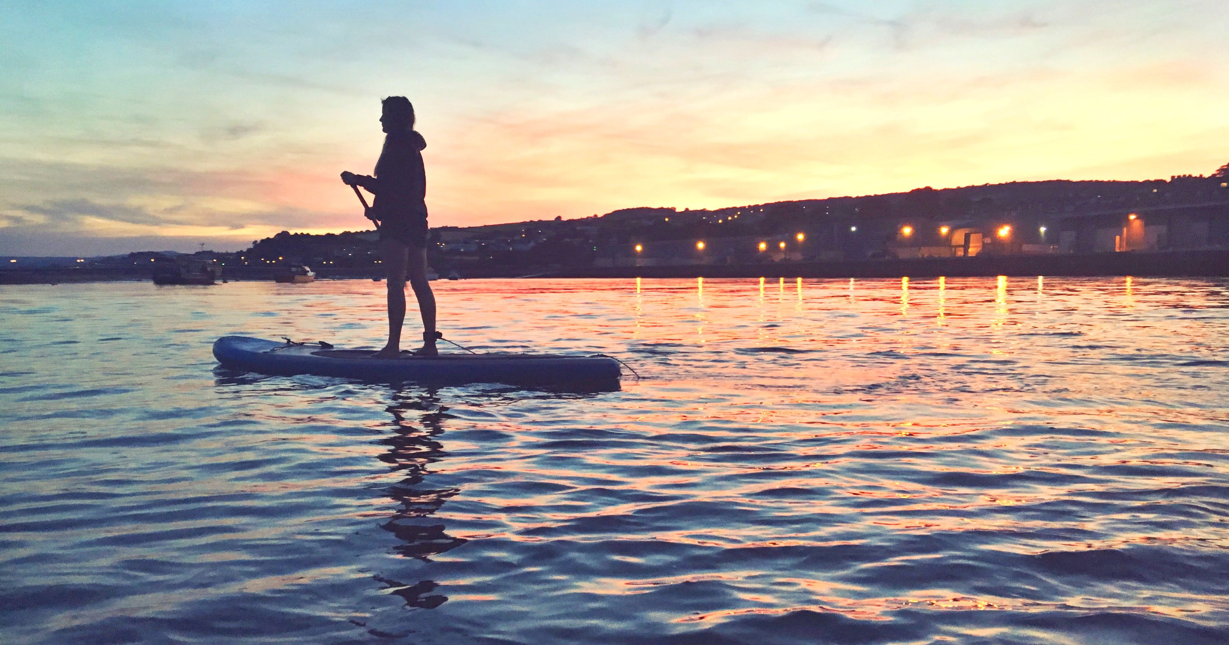 Person paddleboarding on calm water during sunset