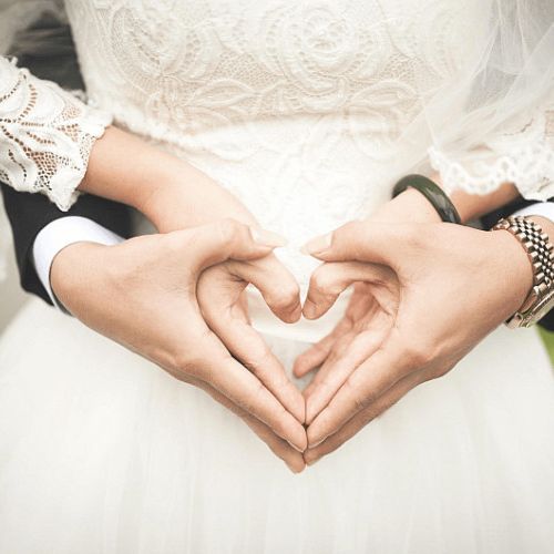 Bride and groom making a heart with their hands in front of the wedding dress