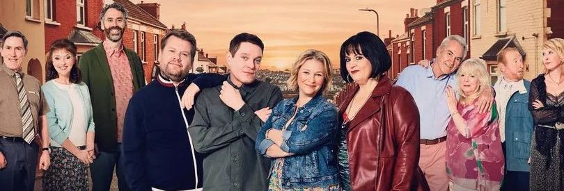 A group of twelve people of different ages, standing on a residential street at sunset. They are dressed casually, posing in pairs or small clusters, smiling warmly.