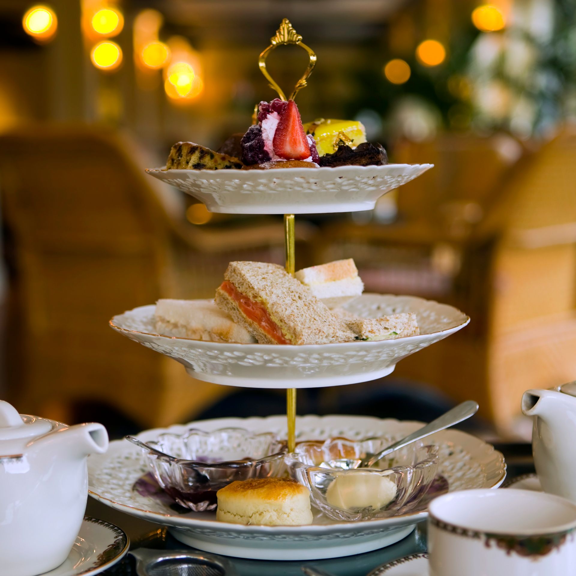 A classic afternoon tea setting with a three-tiered stand featuring finger sandwiches, scones with clotted cream and jam, and an assortment of cakes and pastries.