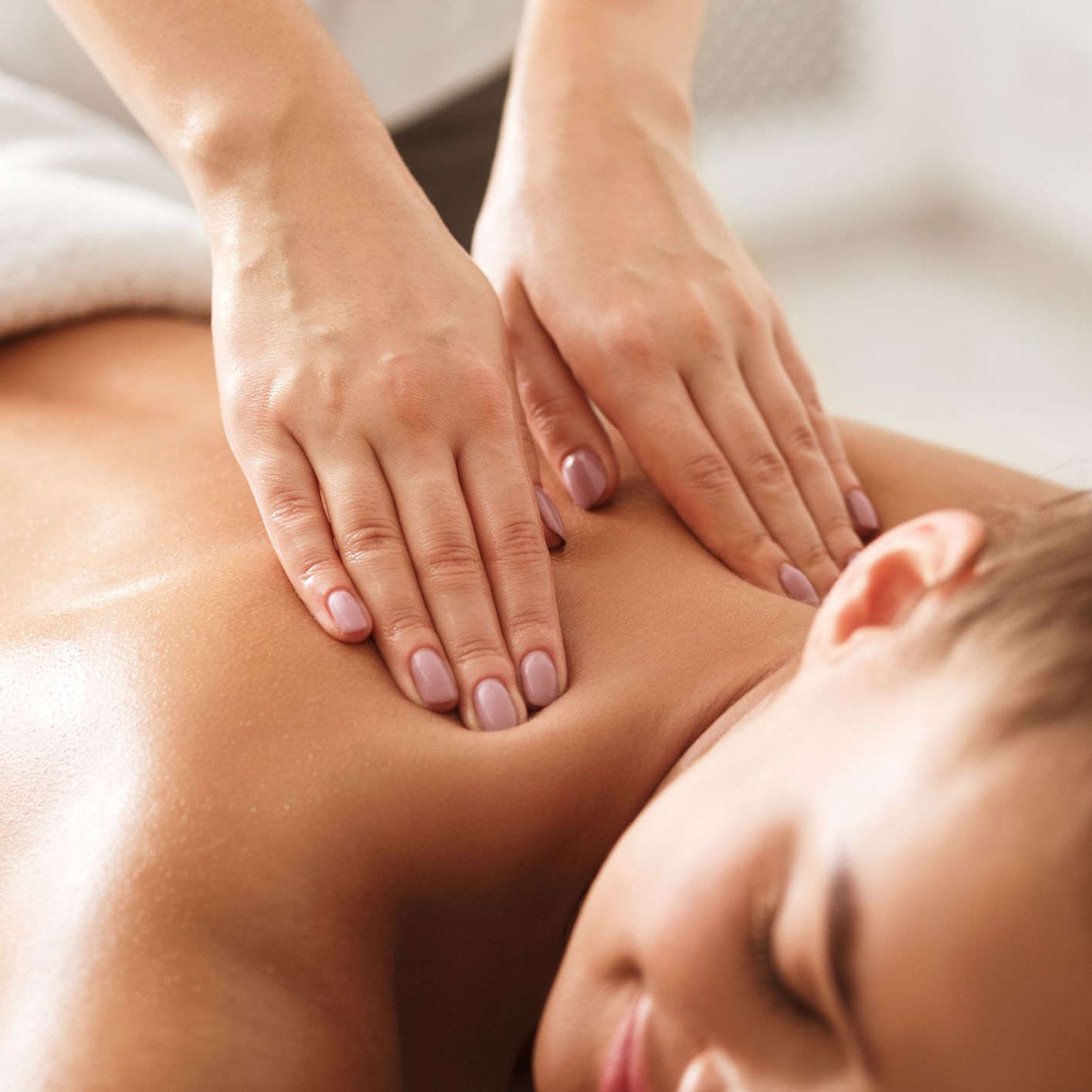 A woman enjoys a relaxing back massage at a spa, with a therapist’s hands applying gentle pressure. The setting is serene, promoting wellness and tranquillity.