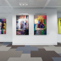 A modern art gallery with abstract paintings displayed on white walls, illuminated by spotlights, with a geometric-patterned carpet adding a contemporary touch.