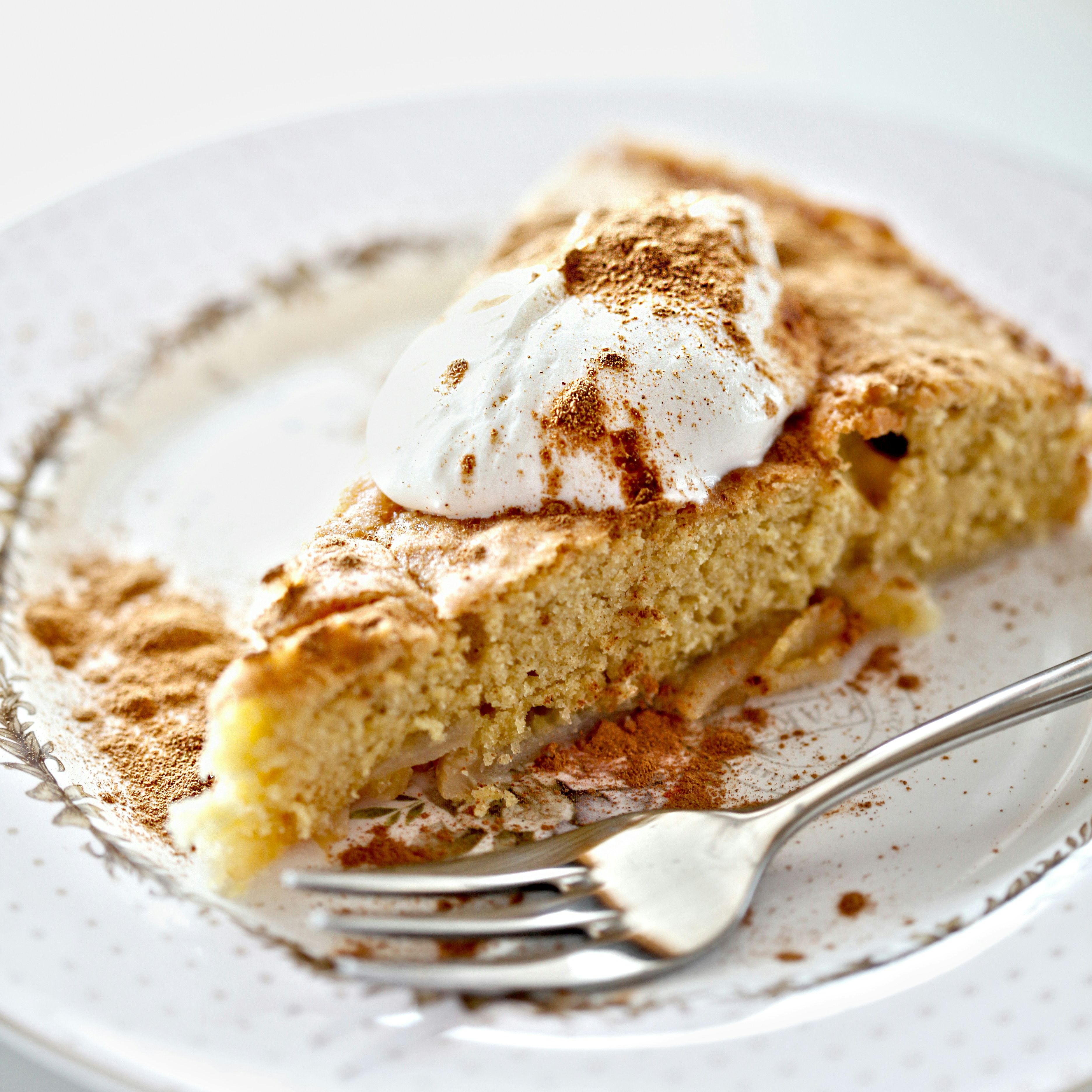Slice of cake topped with whipped cream and cinnamon on a decorative plate