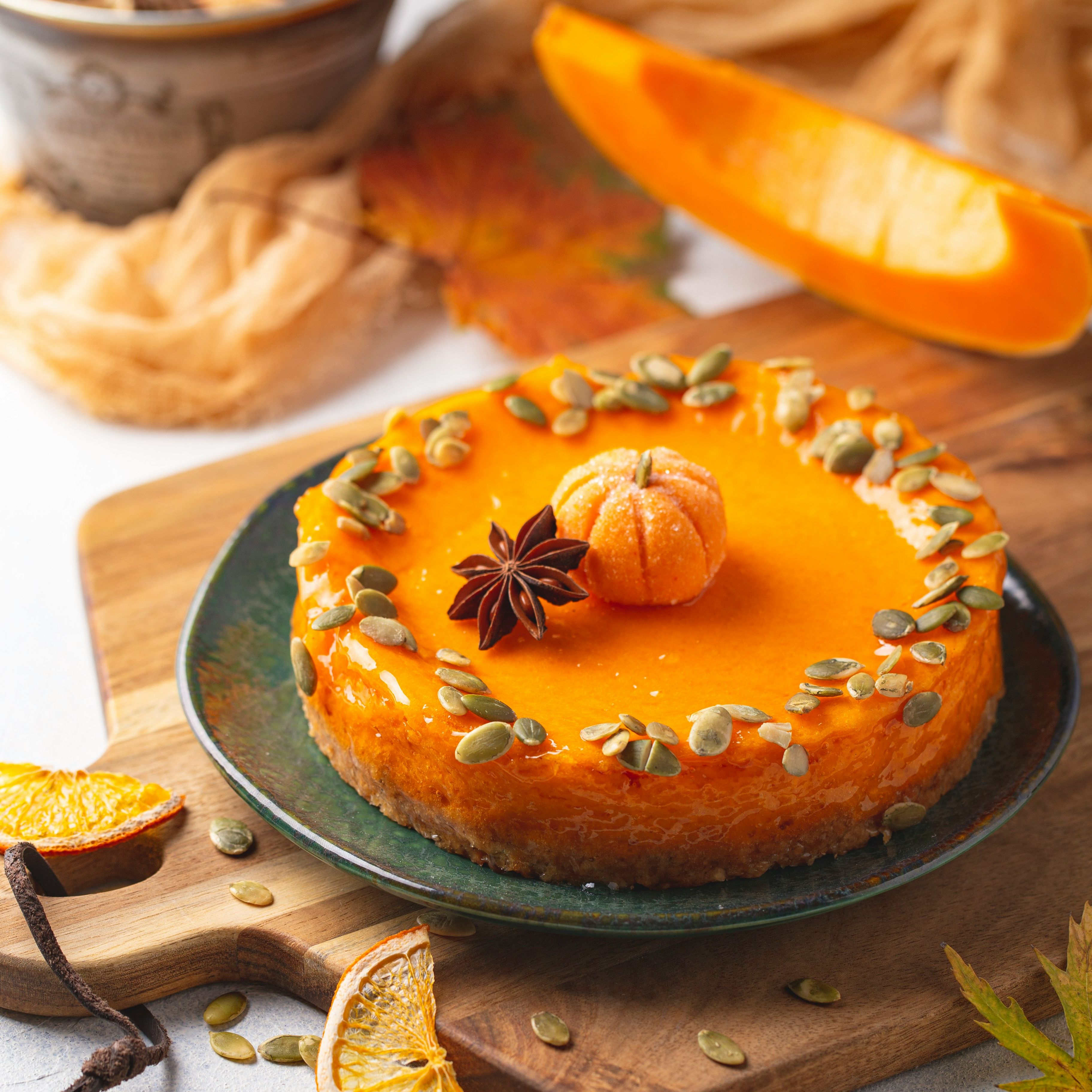 Pumpkin cheesecake decorated with pumpkin seeds, dried orange slices, and an anise star on a wooden board.