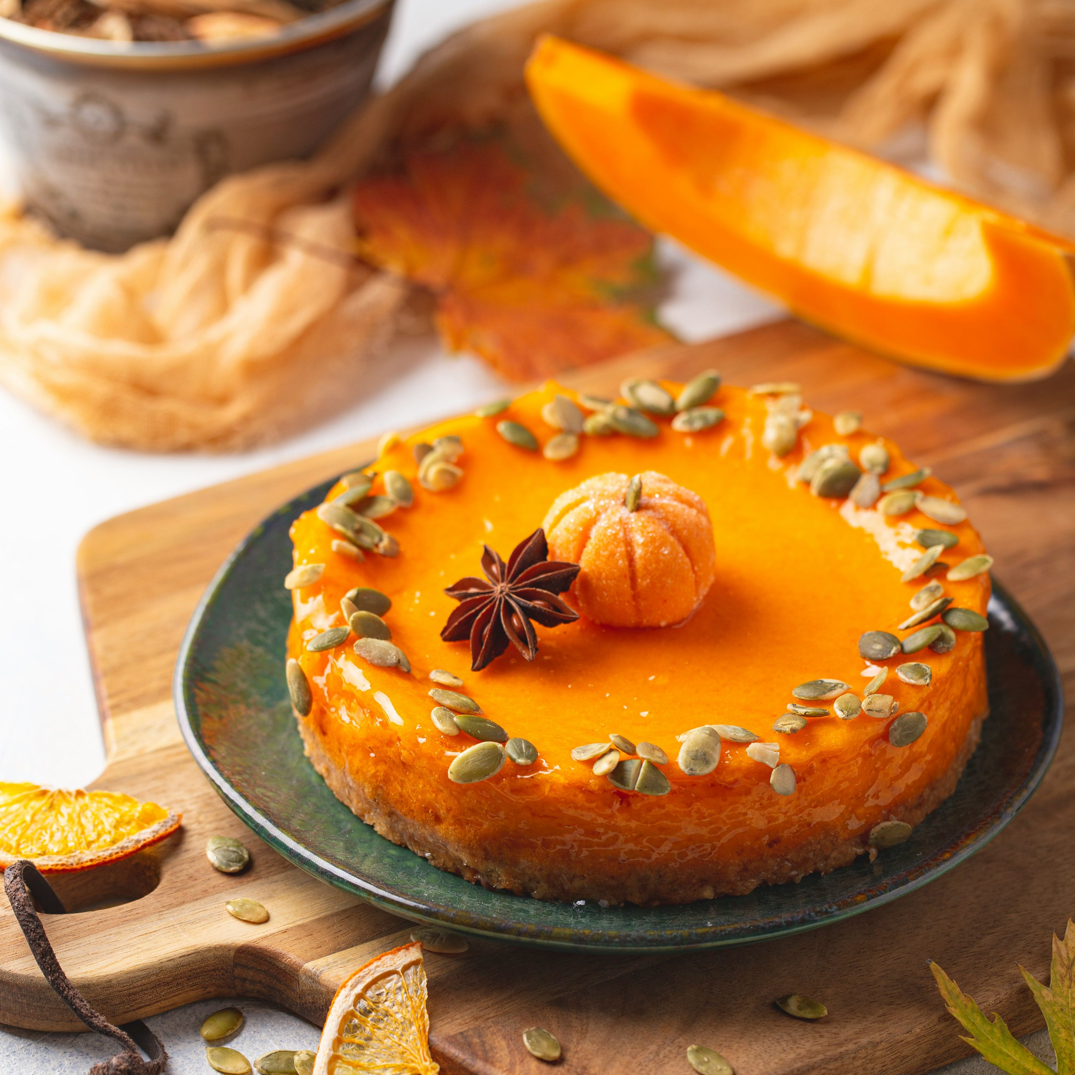 Pumpkin cheesecake decorated with pumpkin seeds, dried orange slices, and an anise star on a wooden board.