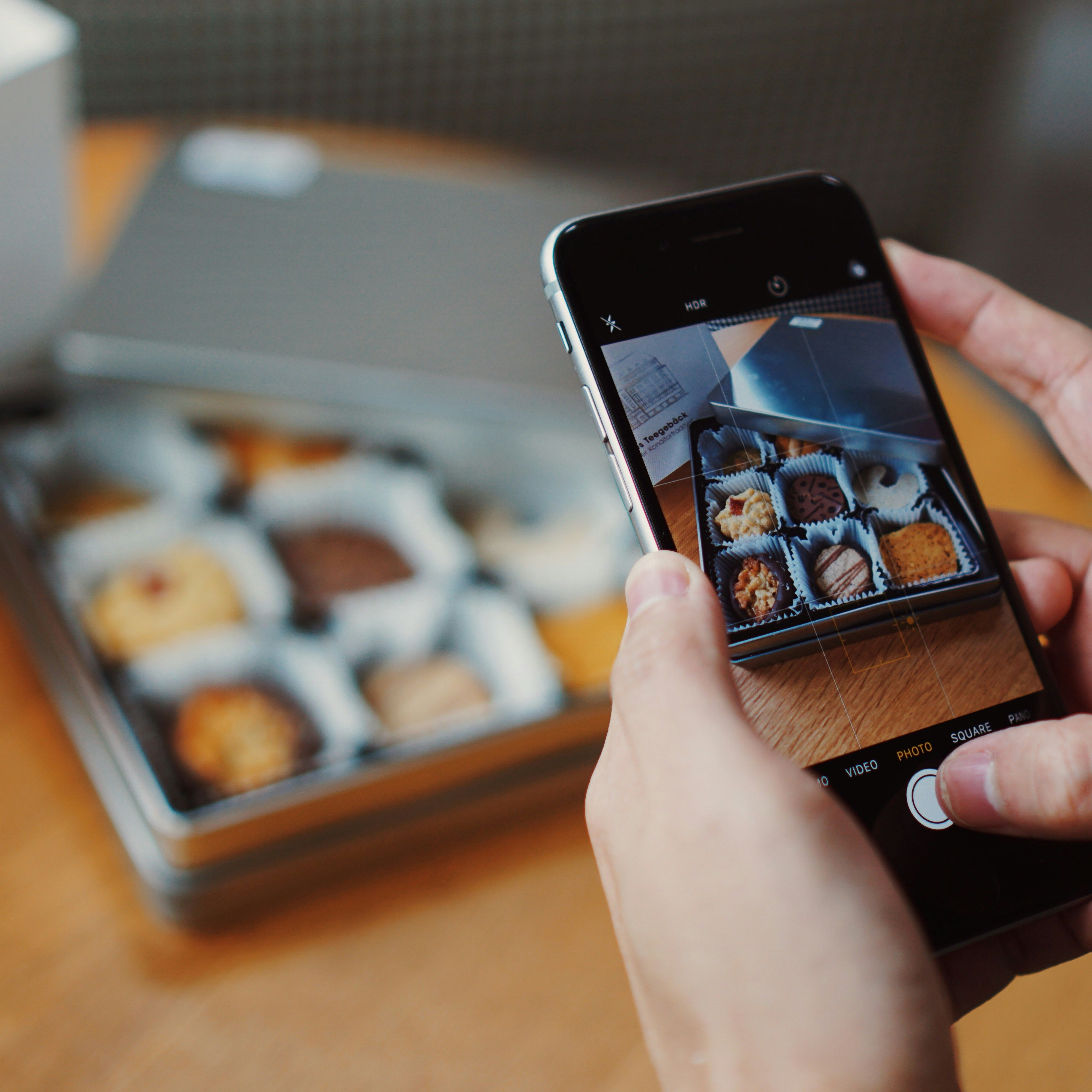 Person taking a photo of assorted cookies in a tin box with a smartphone