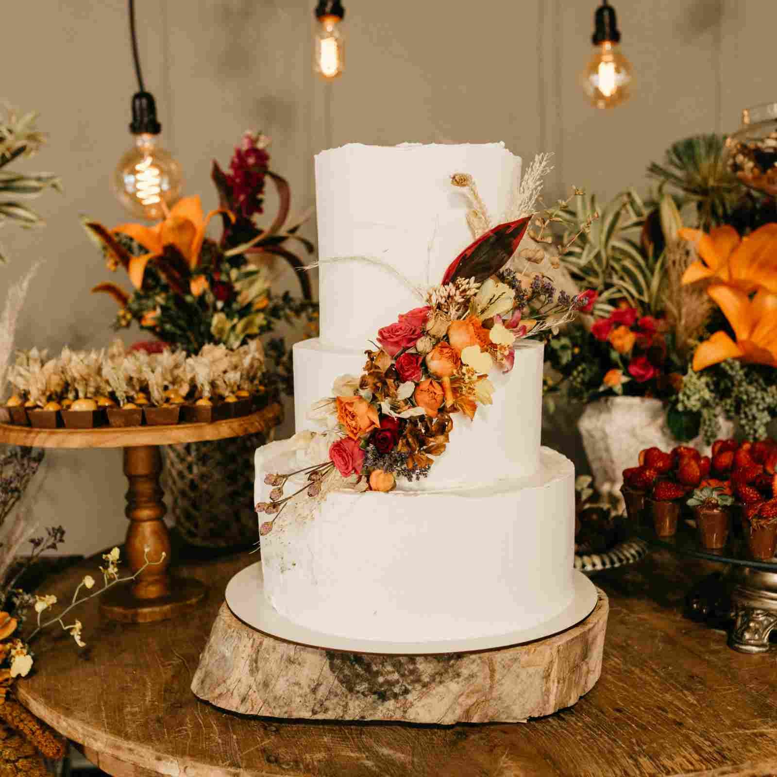 Three-tiered autumn wedding cake decorated with dried flowers and autumnal florals on a wooden table.
