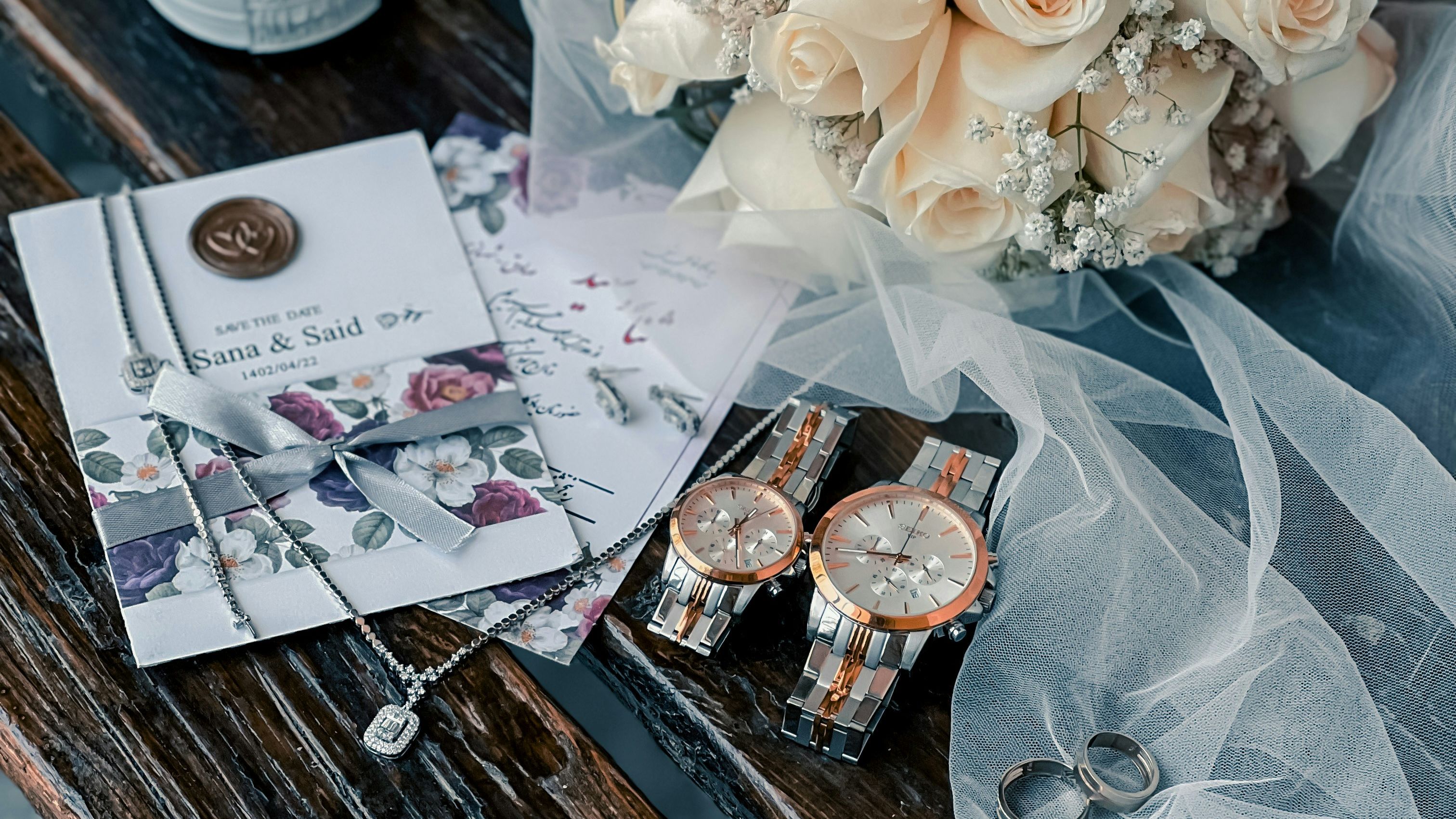 Wedding details on a wooden bench with bridal shoes, bouquet of pale roses, invitation, watches and rings