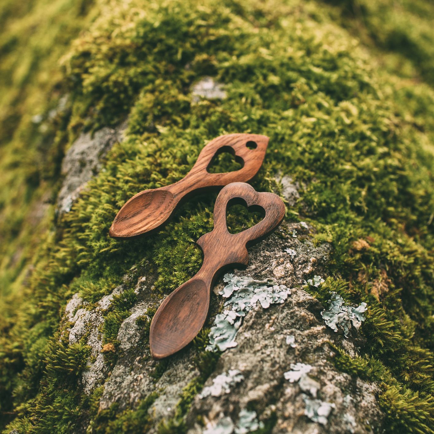 Two wooden spoons with heart-shaped handles on a mossy rock outdoors