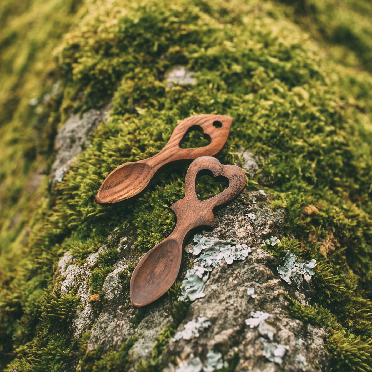Two wooden spoons with heart-shaped handles on a mossy rock outdoors