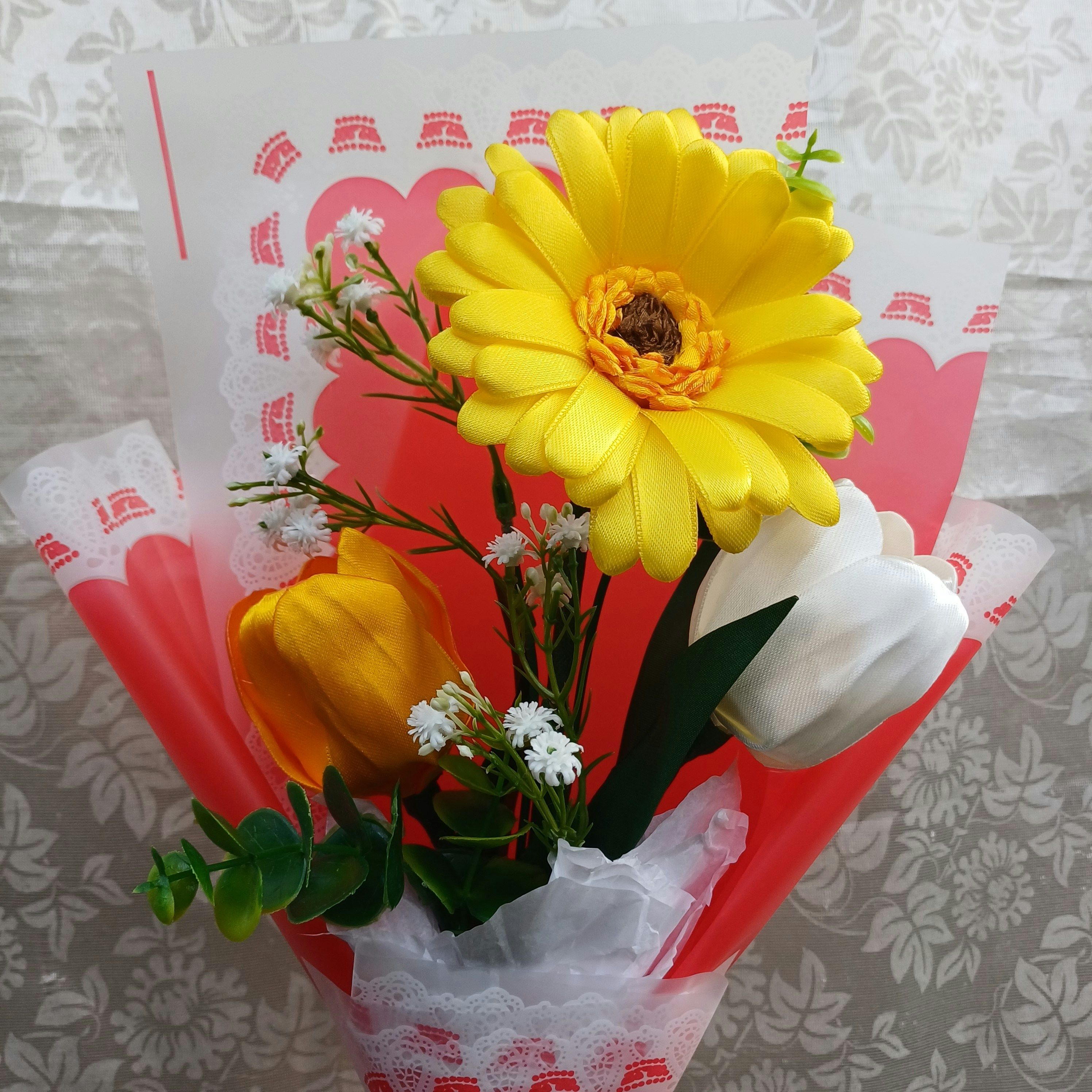 Close-up of a bouquet with a bright yellow daisy, white rose and small white flowers wrapped in pink paper