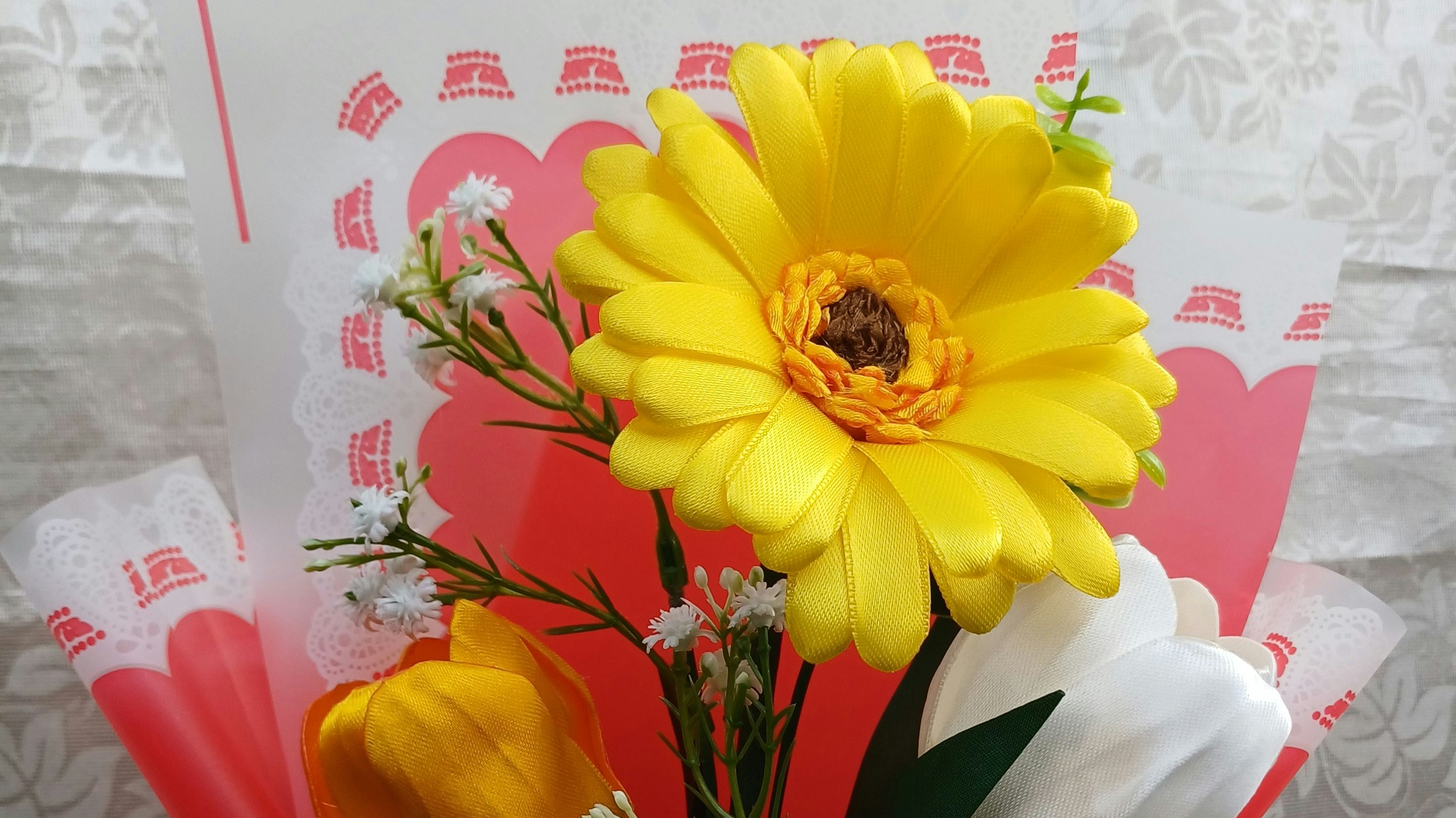 Close-up of a bouquet with a bright yellow daisy, white rose and small white flowers wrapped in pink paper