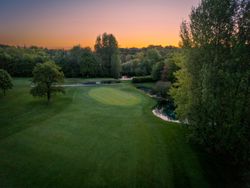 Aerial view of a golf green surrounded by trees at sunset.