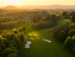 Aerial view of a golf course hole surrounded by trees at sunset
