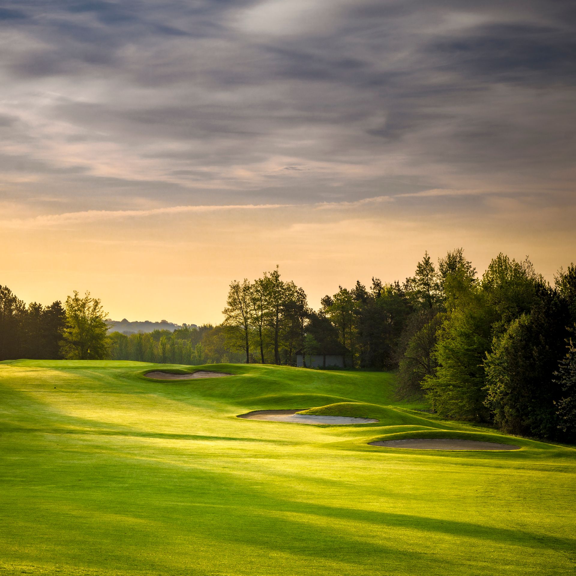 Scenic view of a golf course fairway with sand bunkers and trees during sunset.